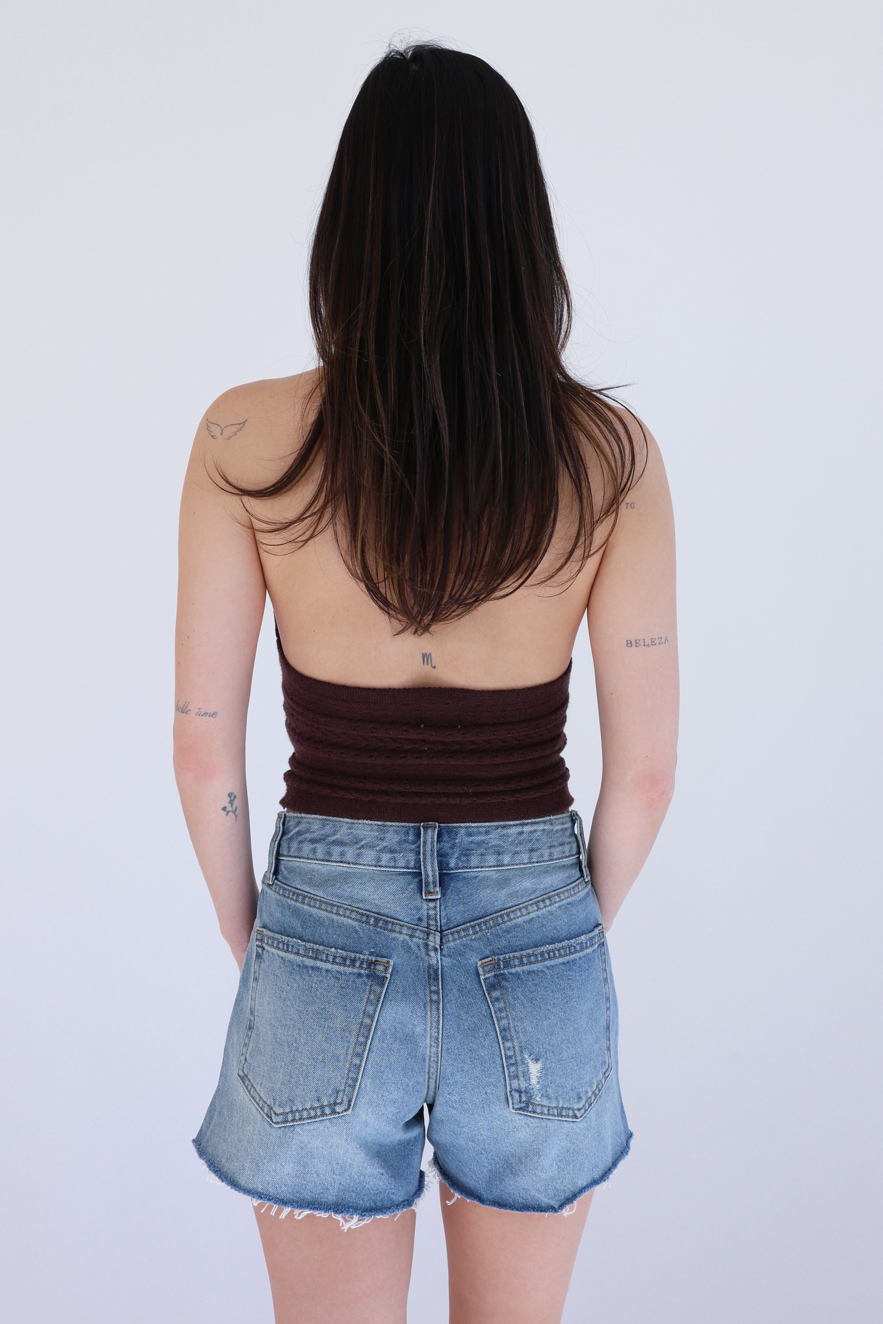 Person wearing a brown tank top and blue denim shorts on a white background