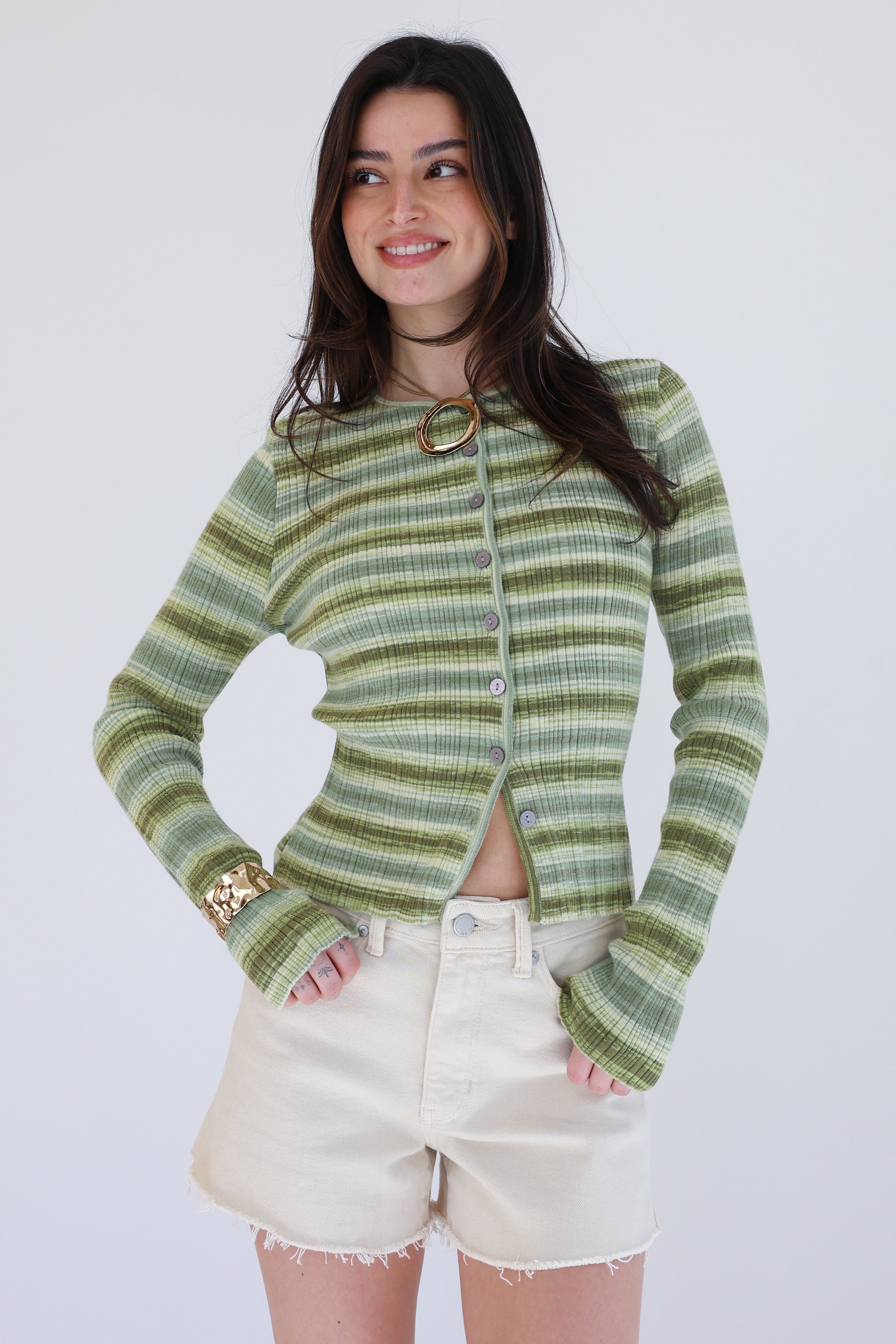 Woman wearing a green striped sweater and white shorts against a plain background