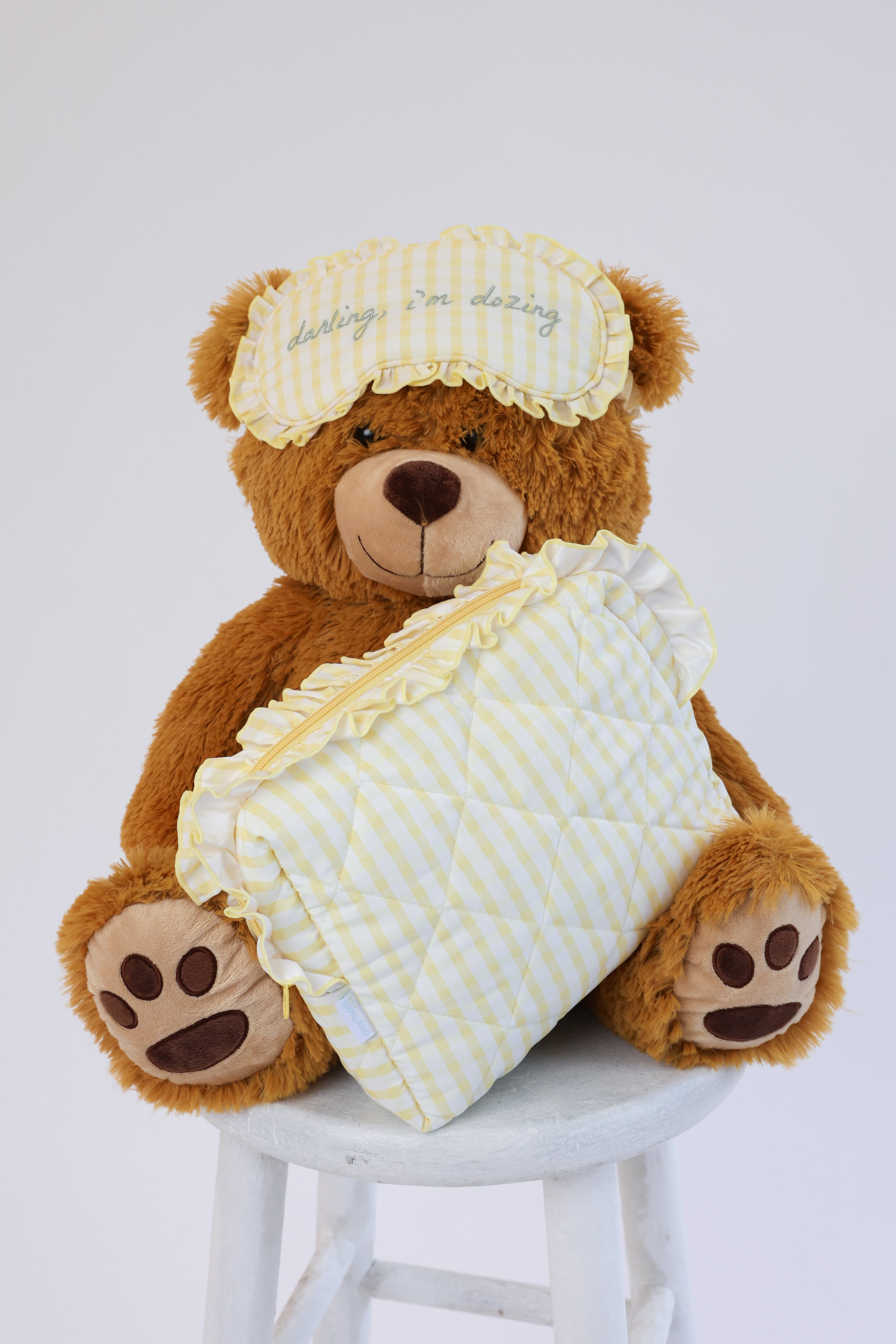 Teddy bear wearing a nightcap and holding a yellow blanket on a white stool.
