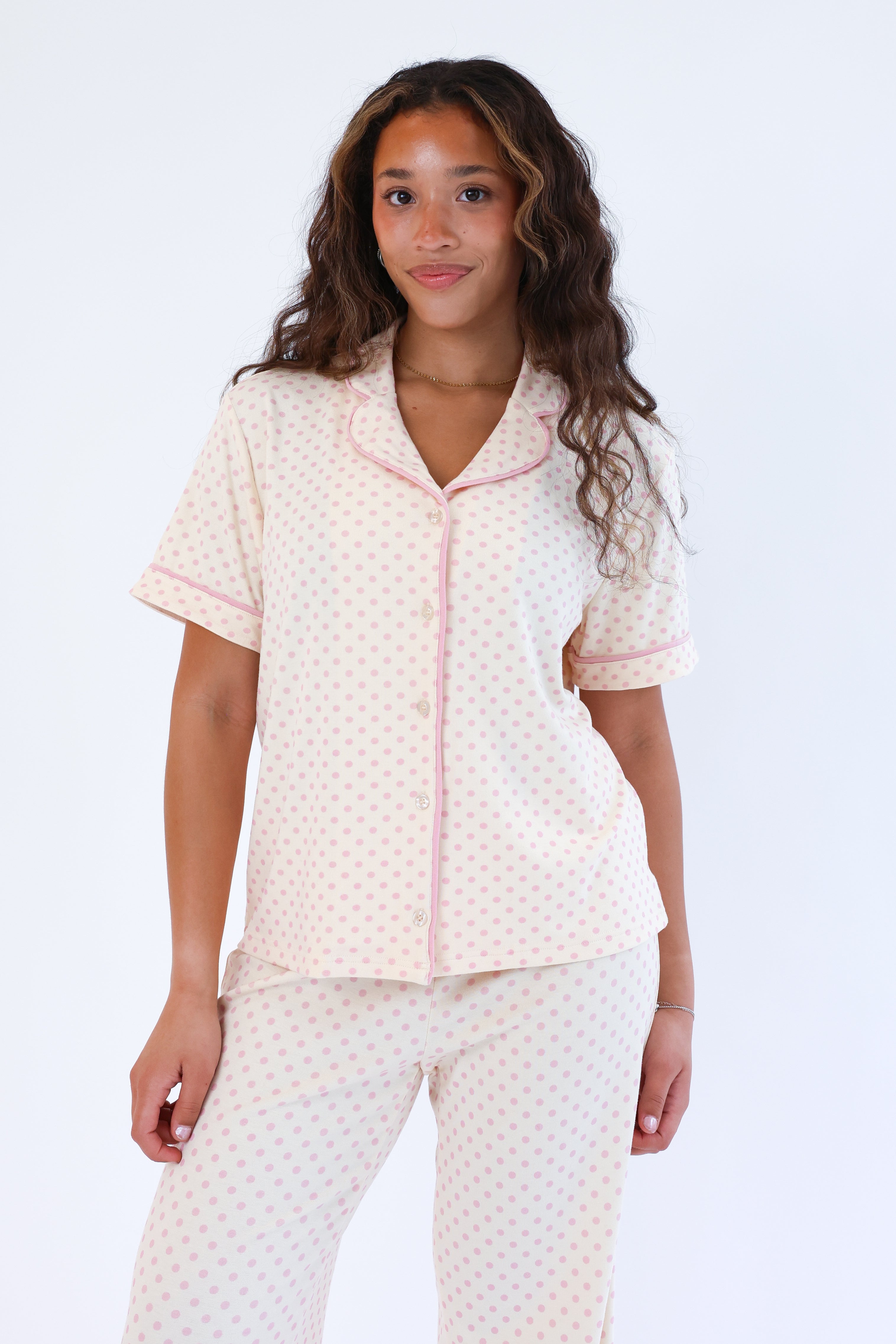 Woman wearing a light pink and white polka dot pajama set on a white background