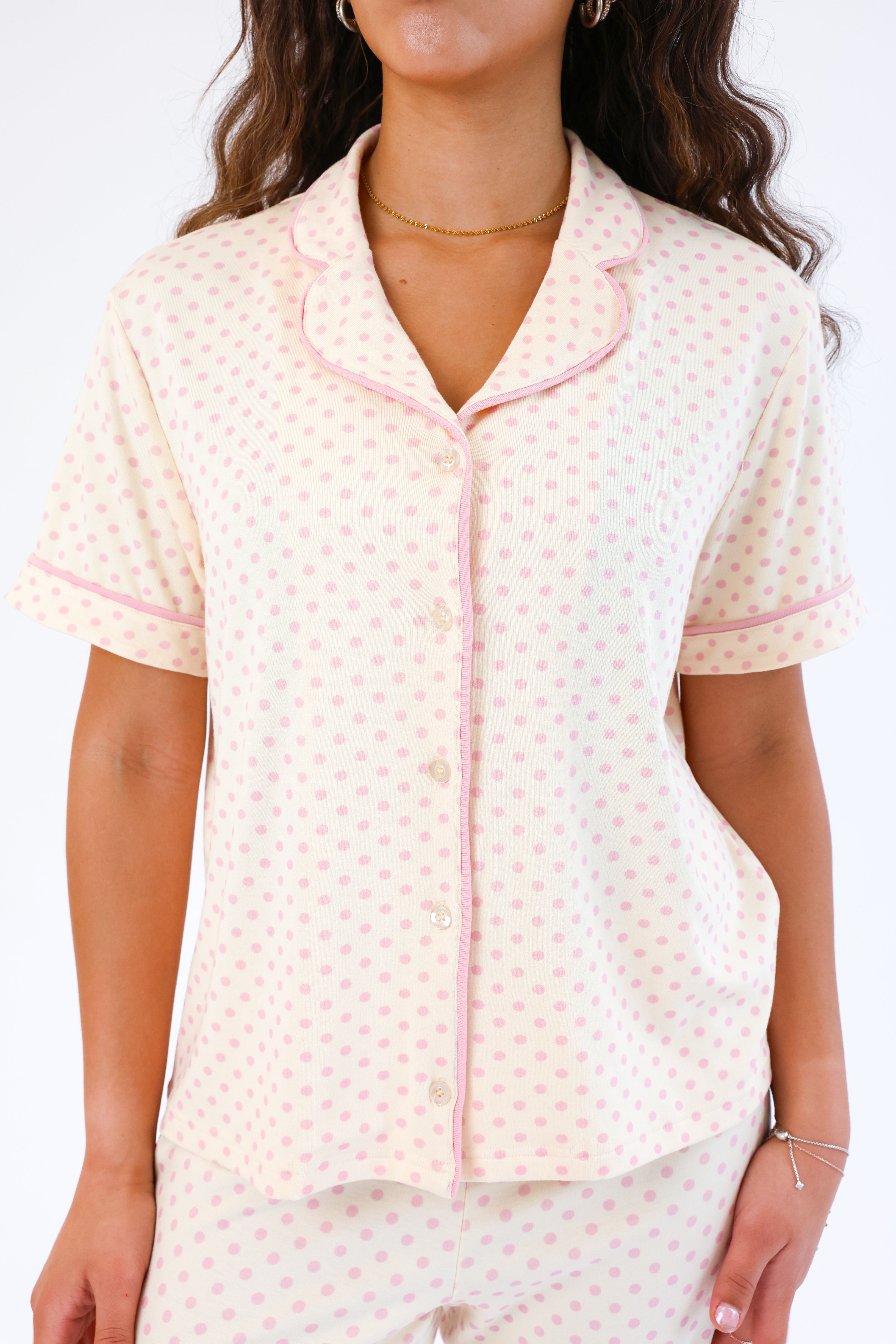 Woman wearing a cream-colored pajama set with pink accents on a white background