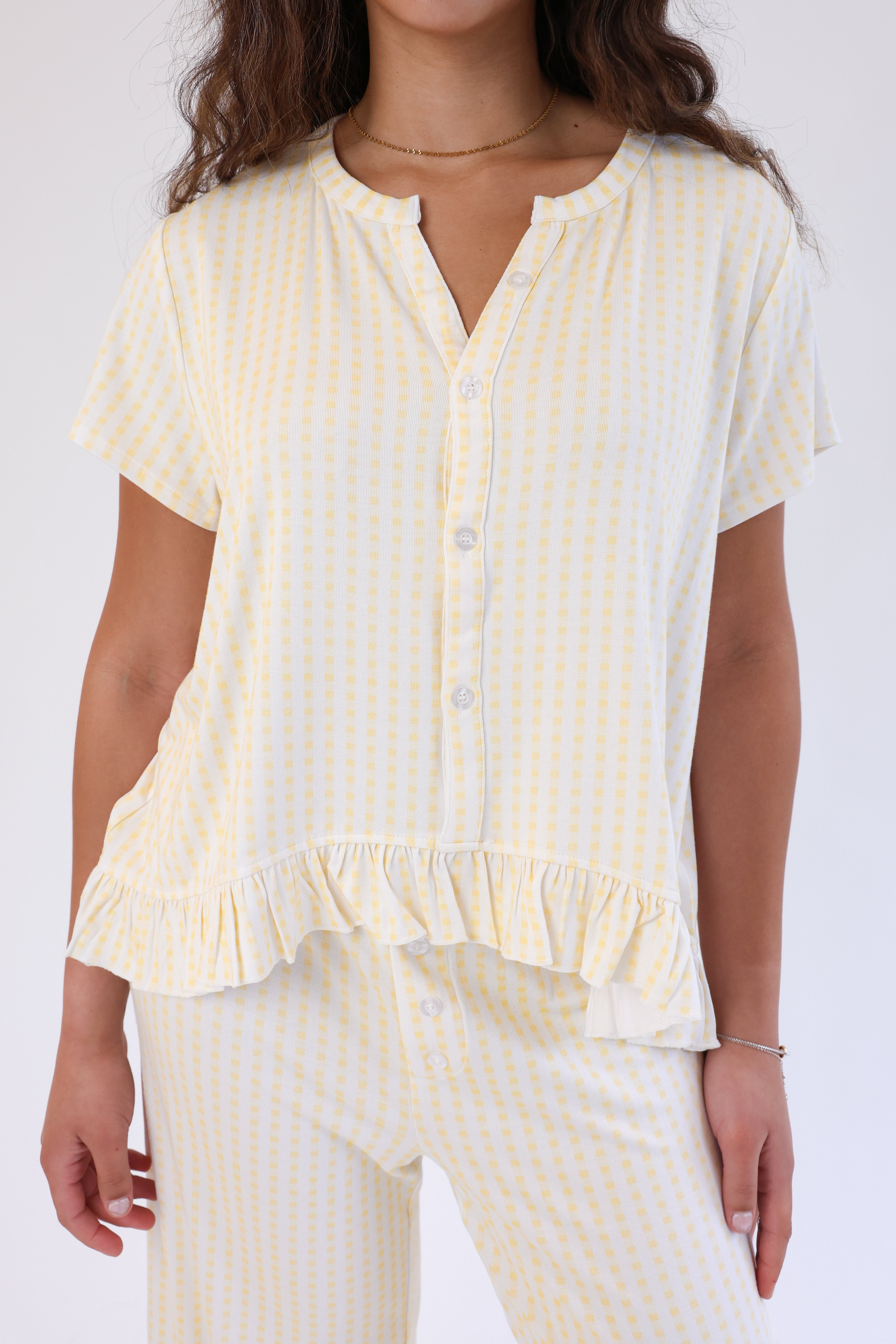 Woman wearing a yellow and white striped shirt with ruffled details on a white background