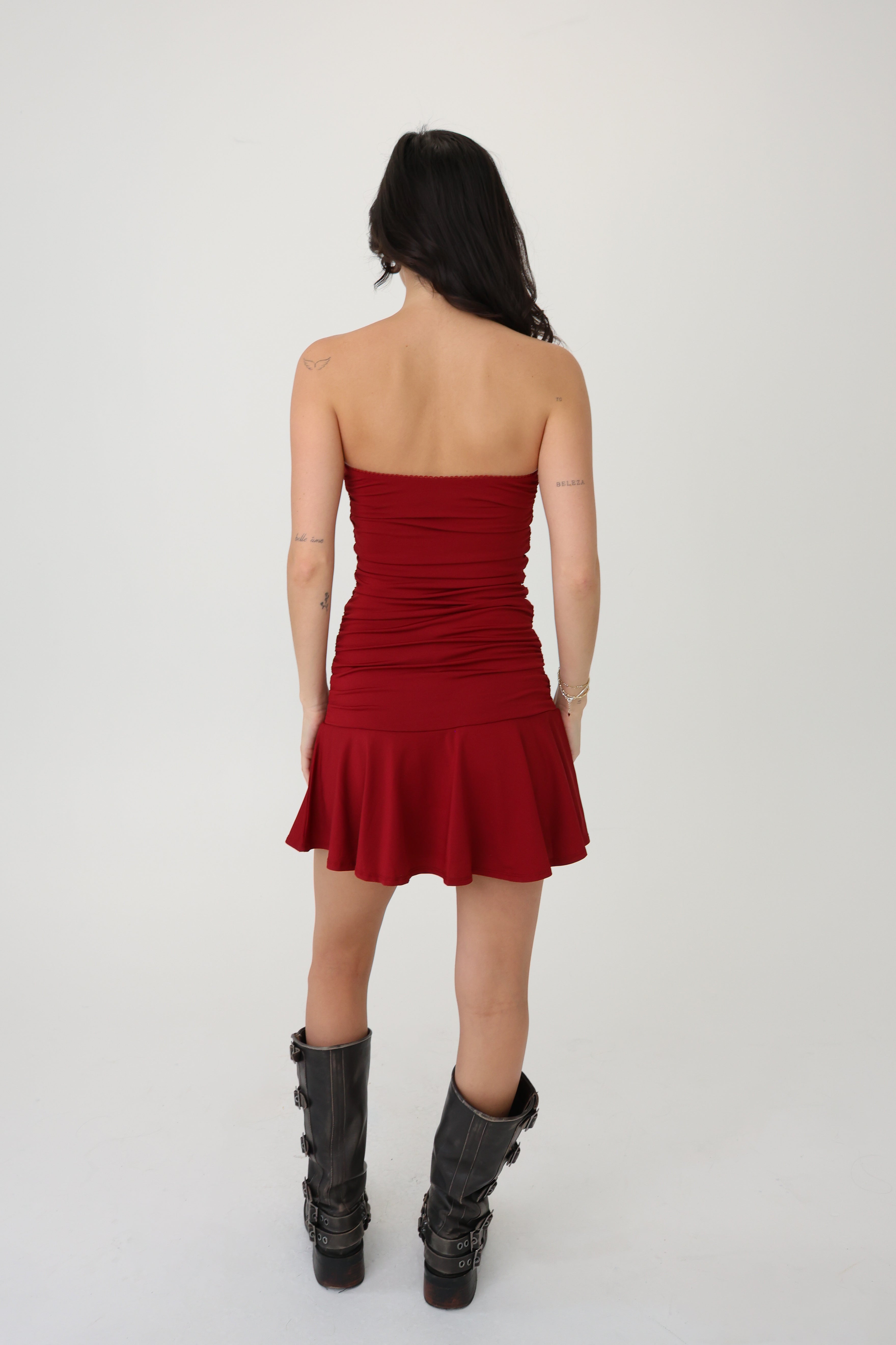 Woman wearing a red strapless dress with black high-heeled boots on a white background
