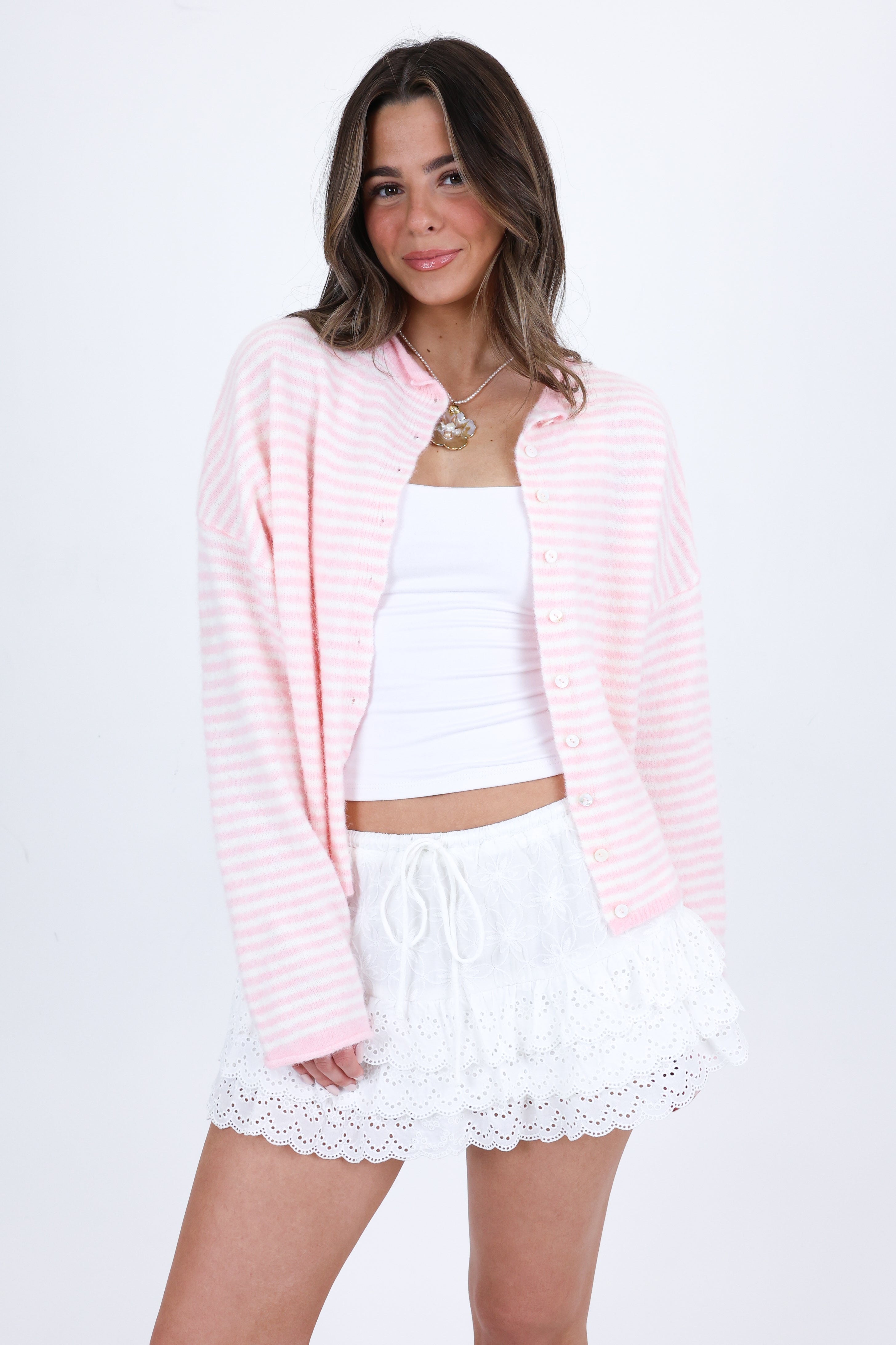 Woman wearing a pink cardigan, white top, and white shorts with lace trim on a white background