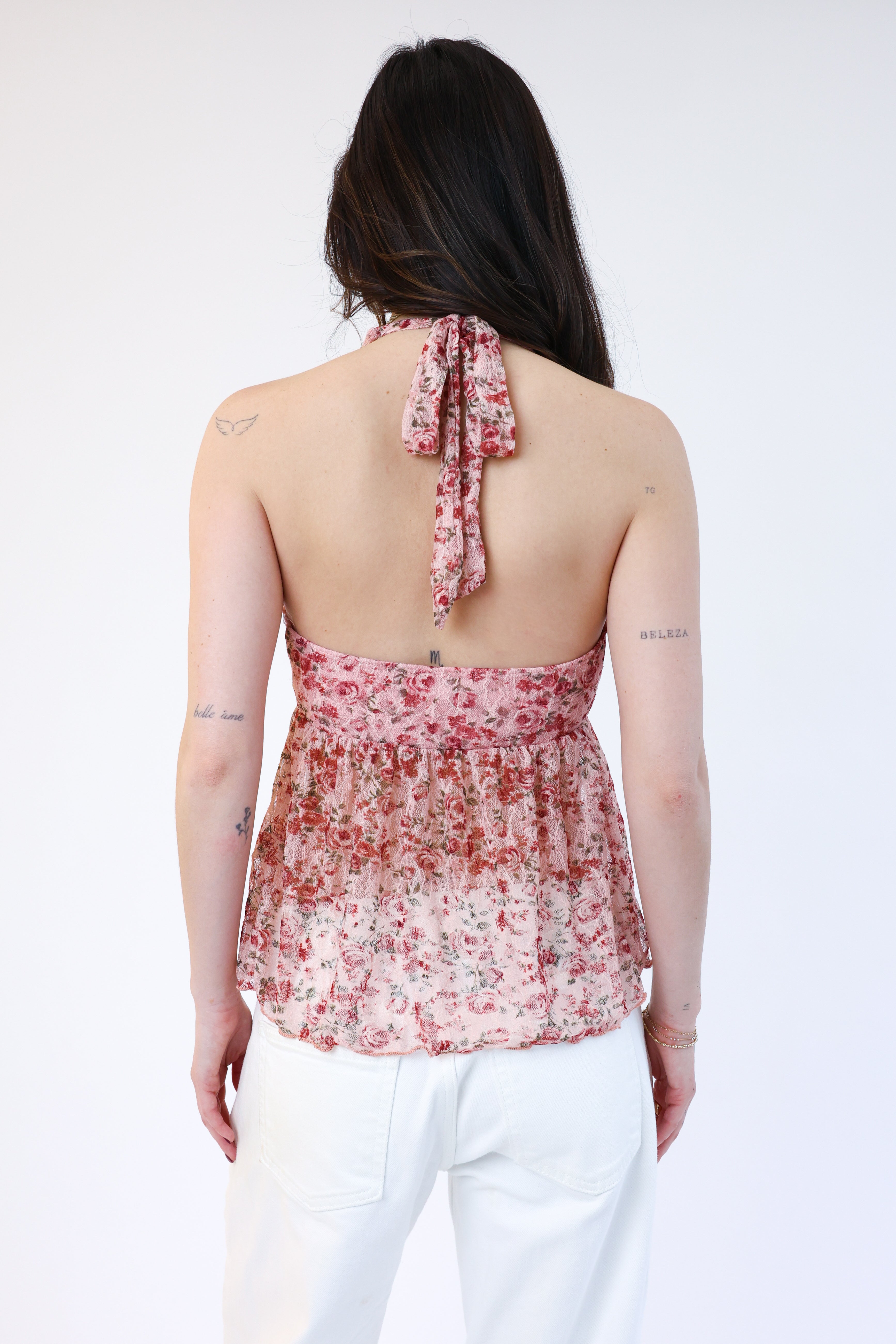 Woman wearing a floral halter top with white pants on a white background