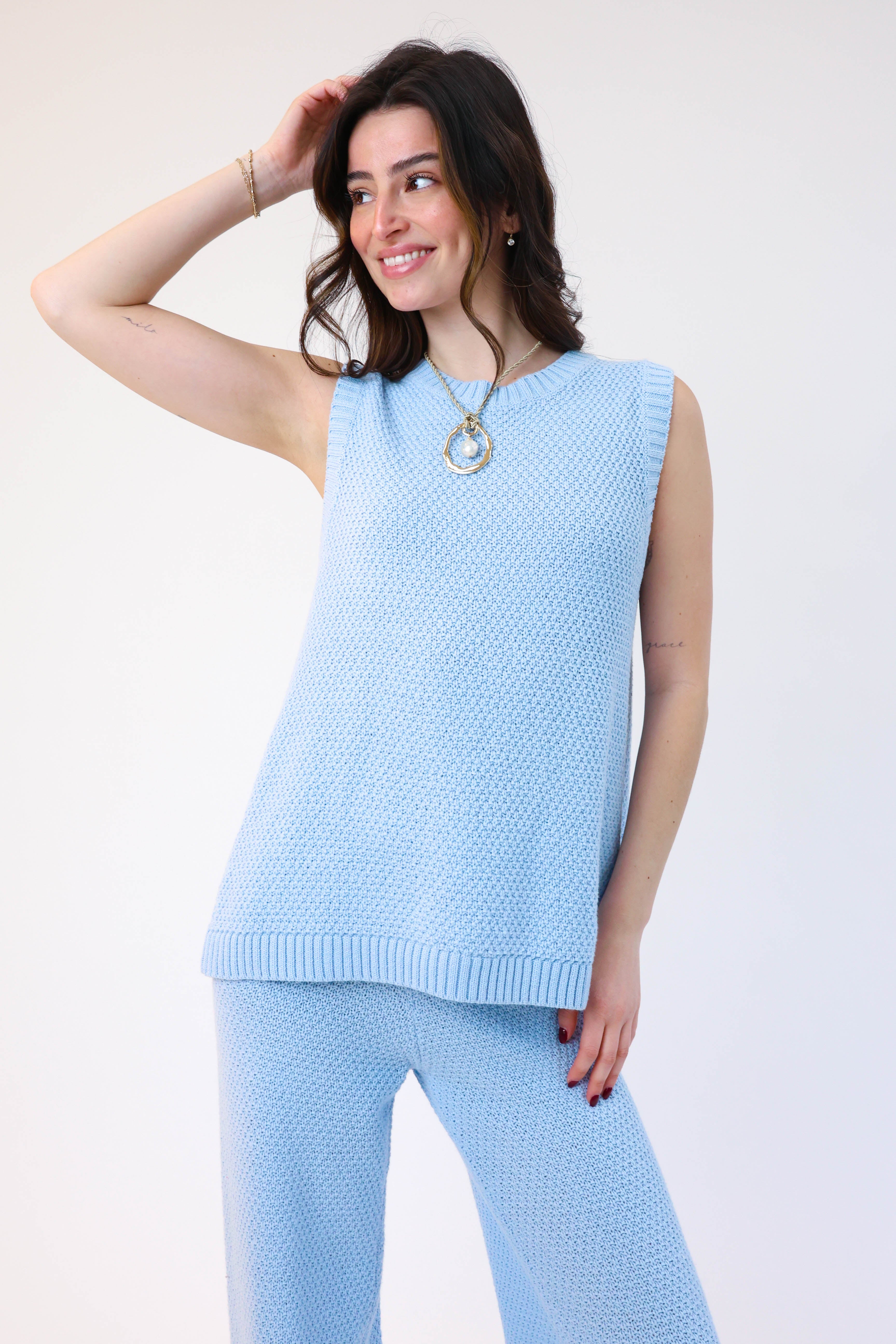 Woman wearing a light blue sleeveless top and pants on a white background
