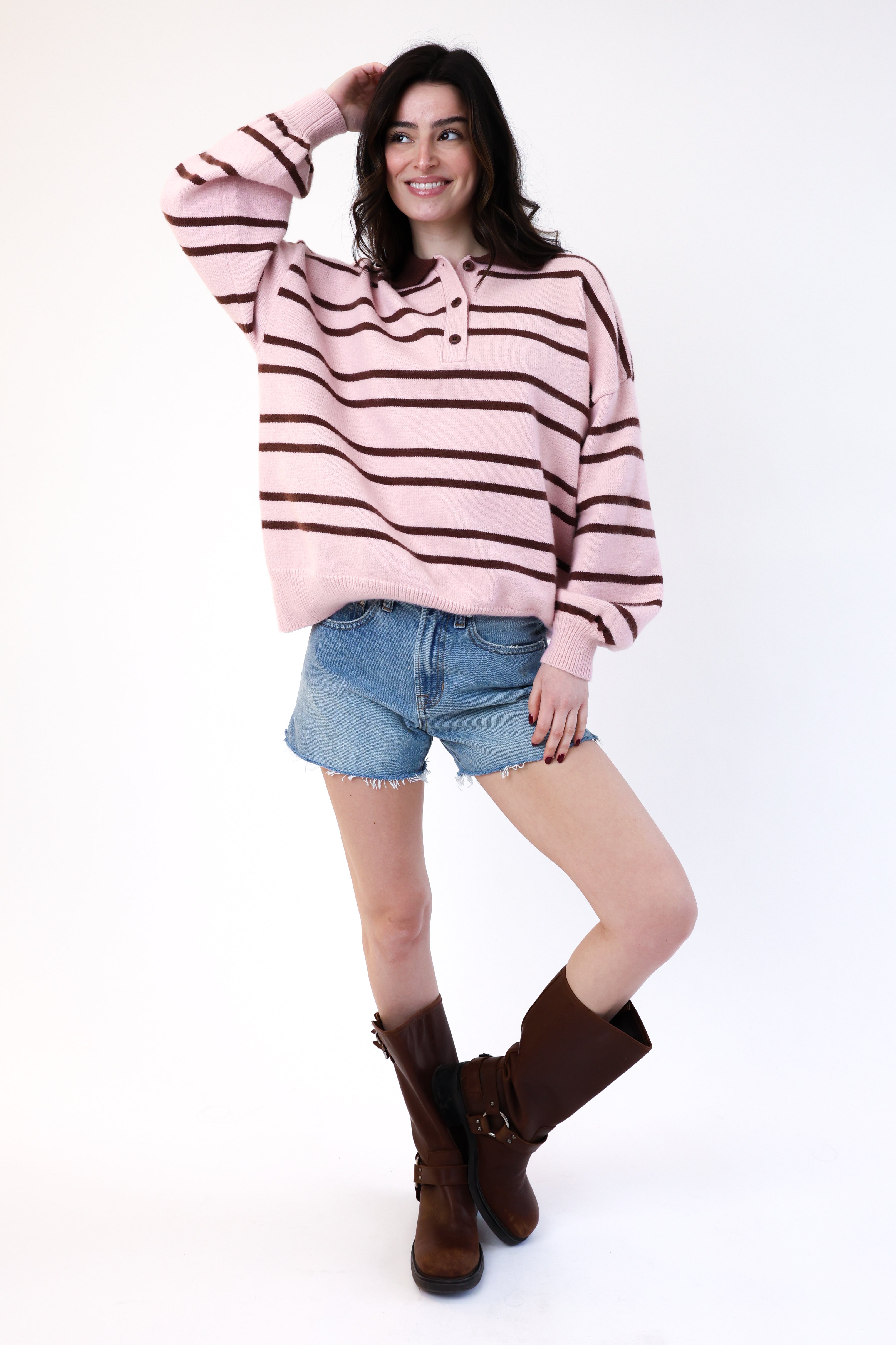 Woman wearing a pink and brown striped sweater with denim shorts and brown boots on a white background