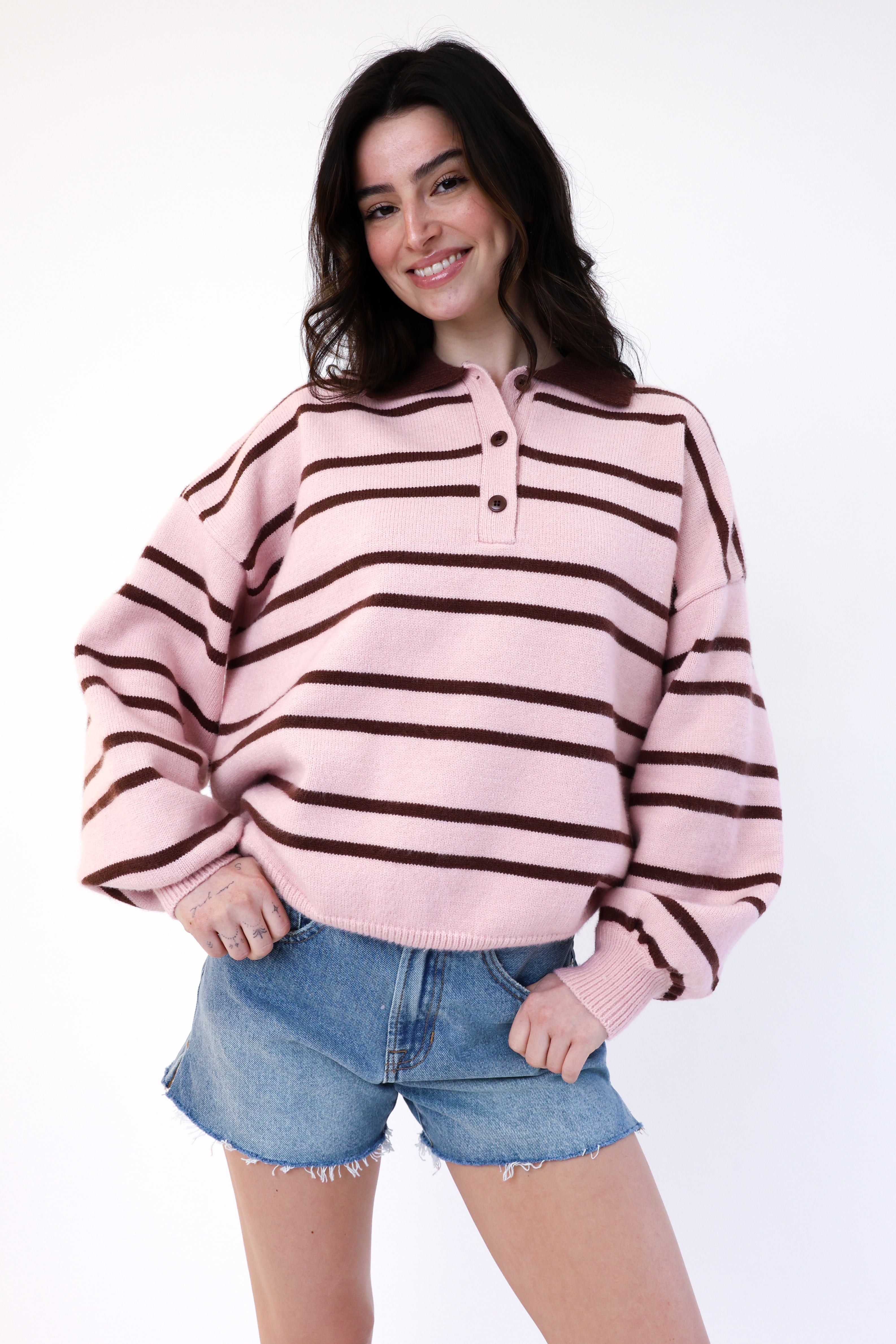 Woman wearing a pink and brown striped sweater with denim shorts on a white background