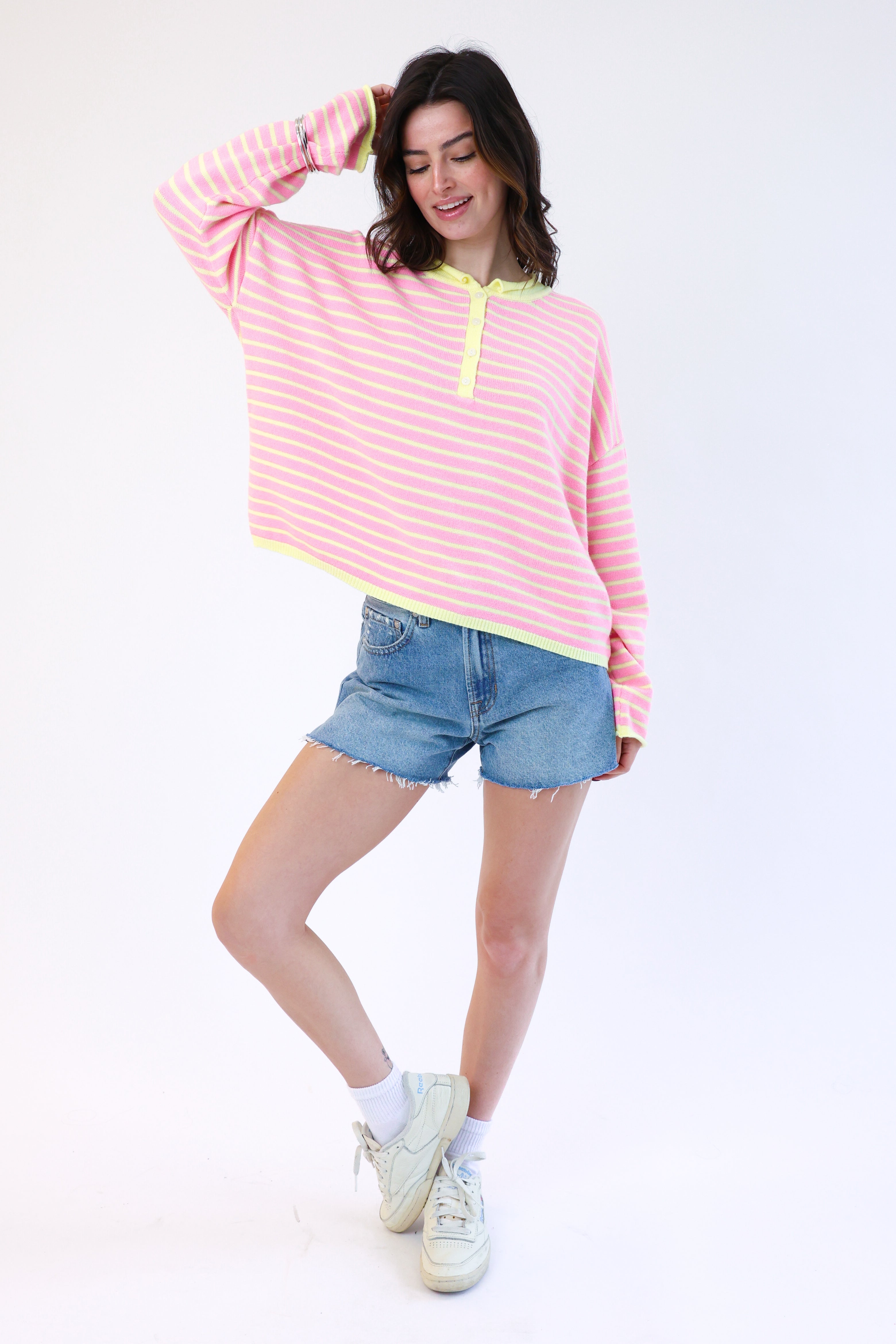 Woman wearing a pink and yellow striped shirt with denim shorts on a white background