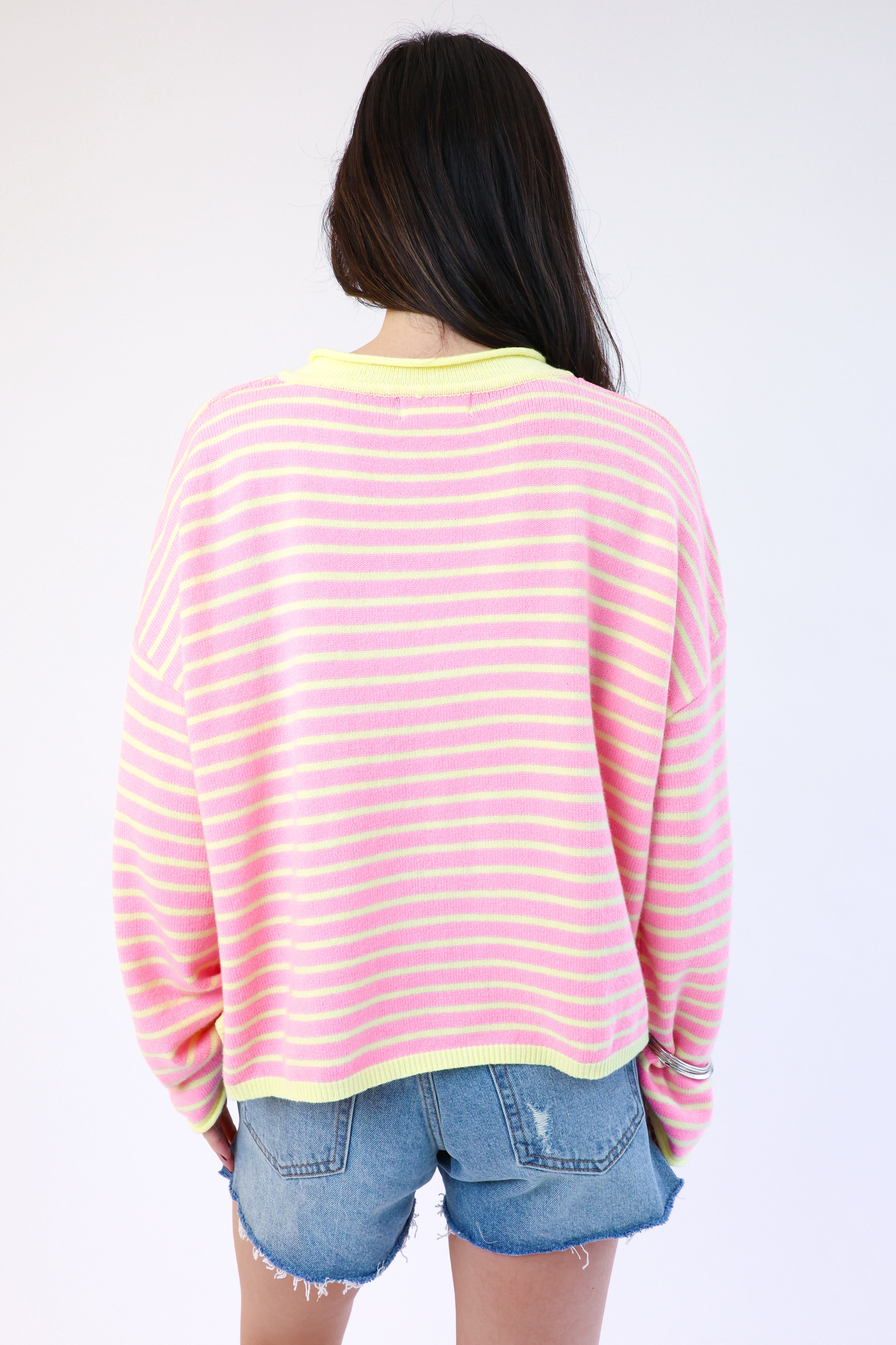 Person wearing a pink and yellow striped sweater with denim shorts on a white background