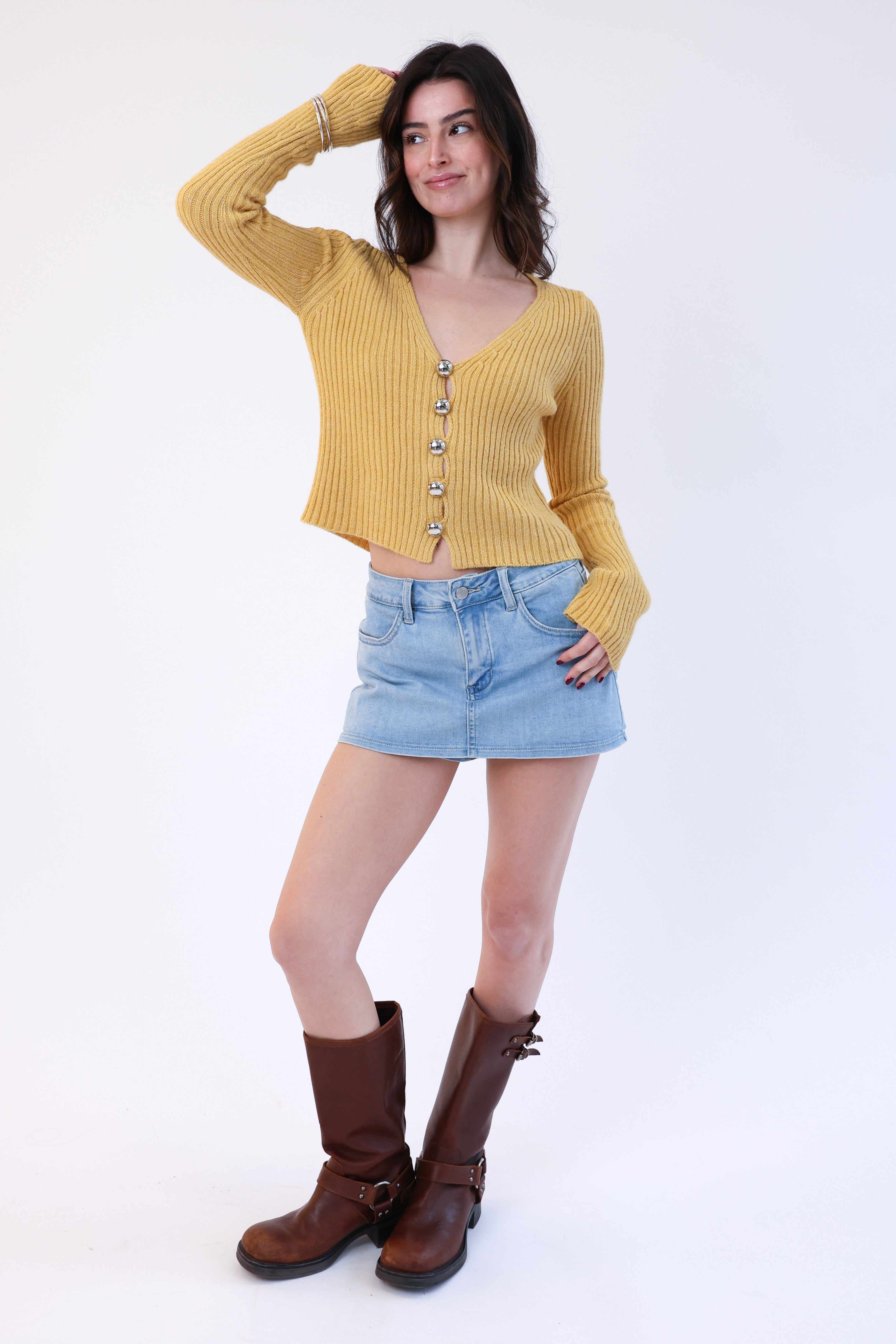 Woman wearing a yellow cardigan, denim shorts, and brown boots on a white background