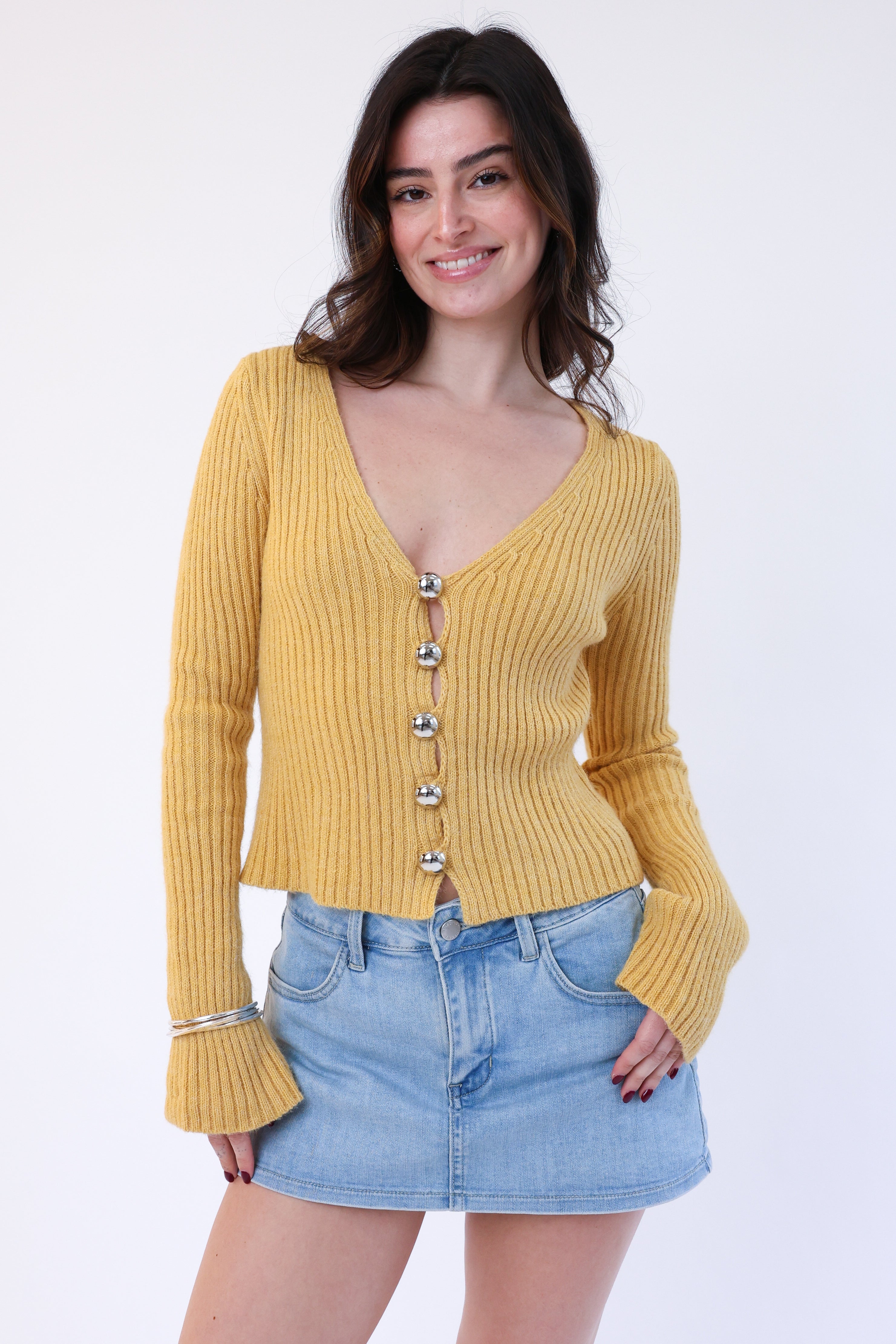 Woman wearing a mustard yellow ribbed sweater with button details and a denim skirt on a white background