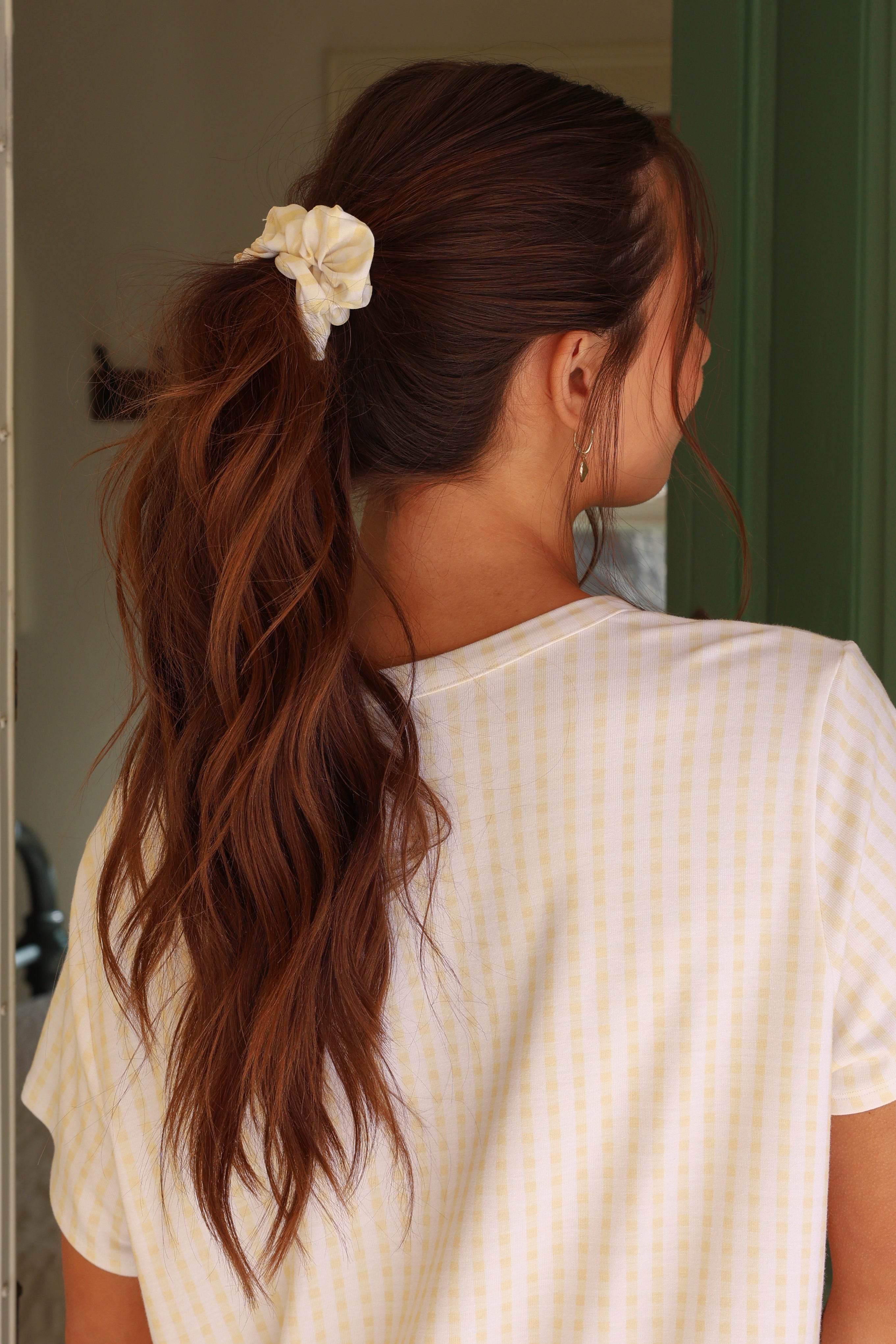 Woman with long brown hair tied back with a white flower accessory, wearing a white t-shirt.
