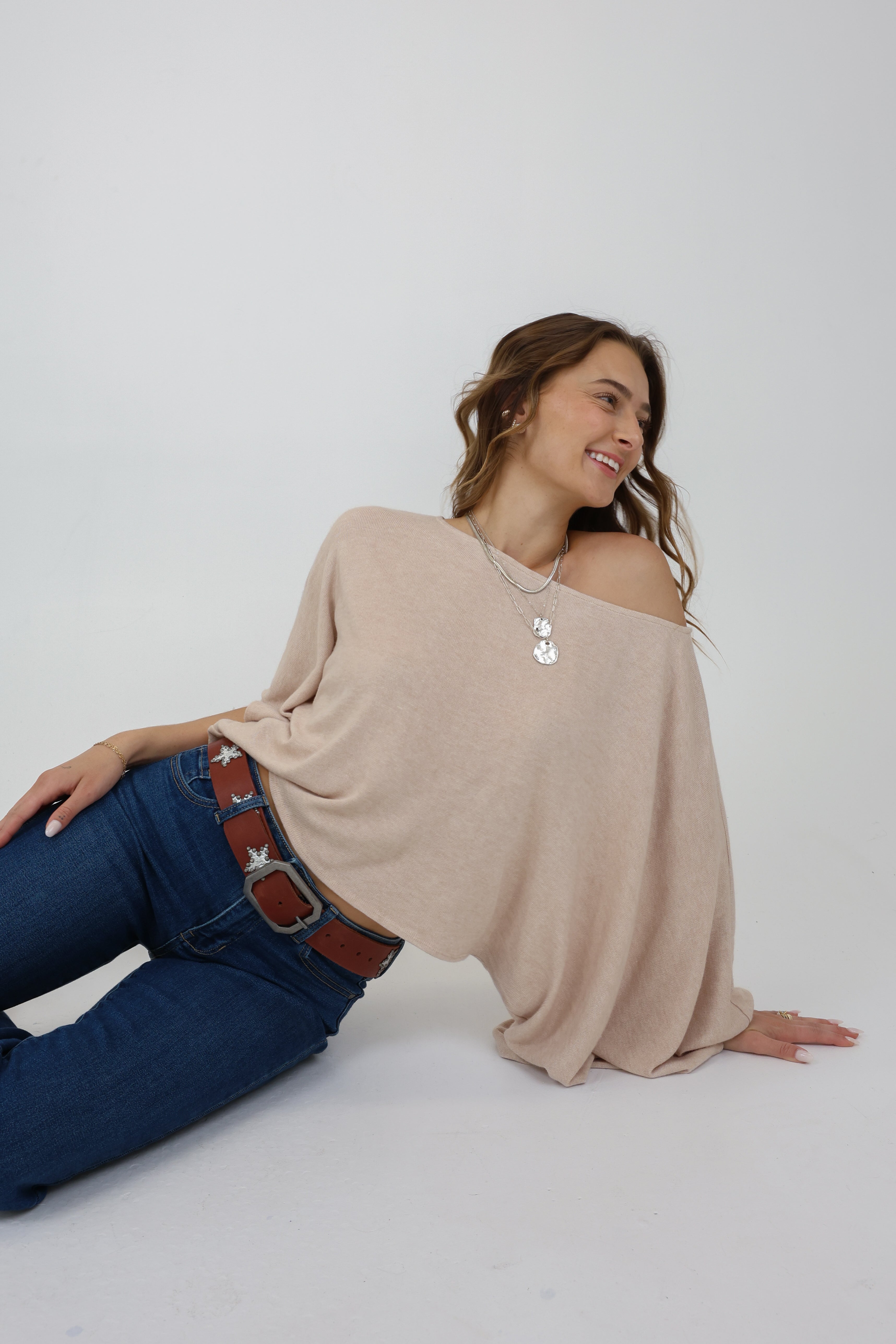 Woman wearing a beige off-shoulder top and blue jeans on a white background