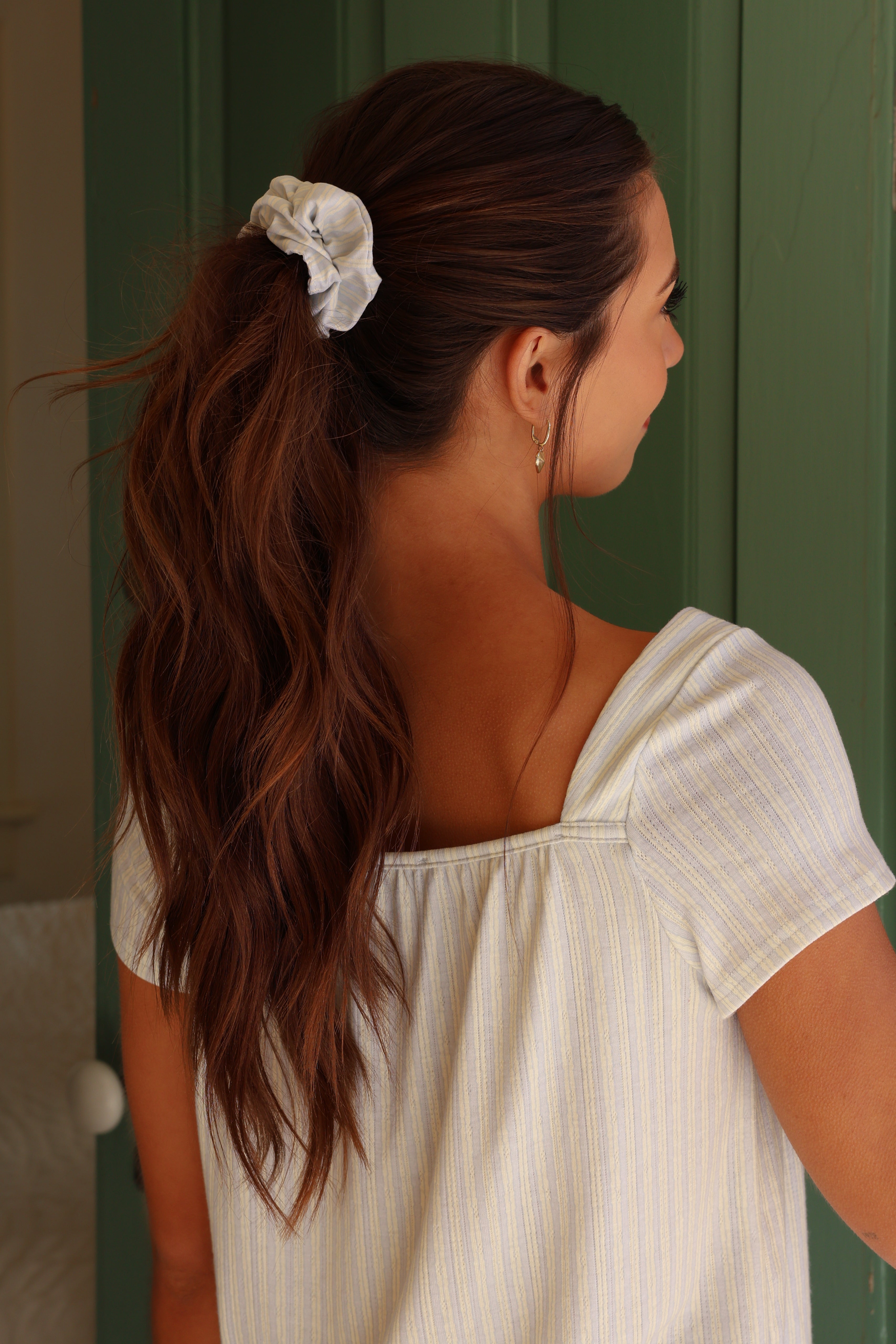 Woman with a ponytail wearing a white blouse against a green background