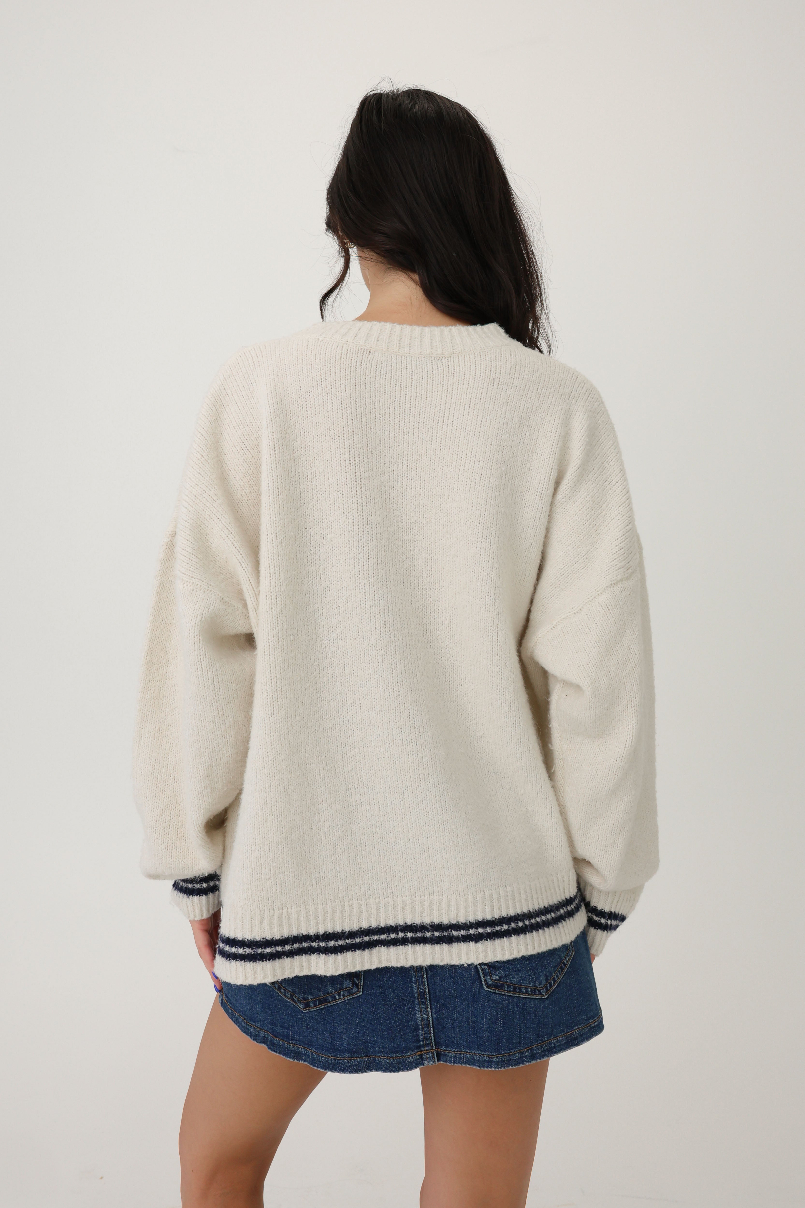 Person wearing a cream sweater with a blue skirt on a white background