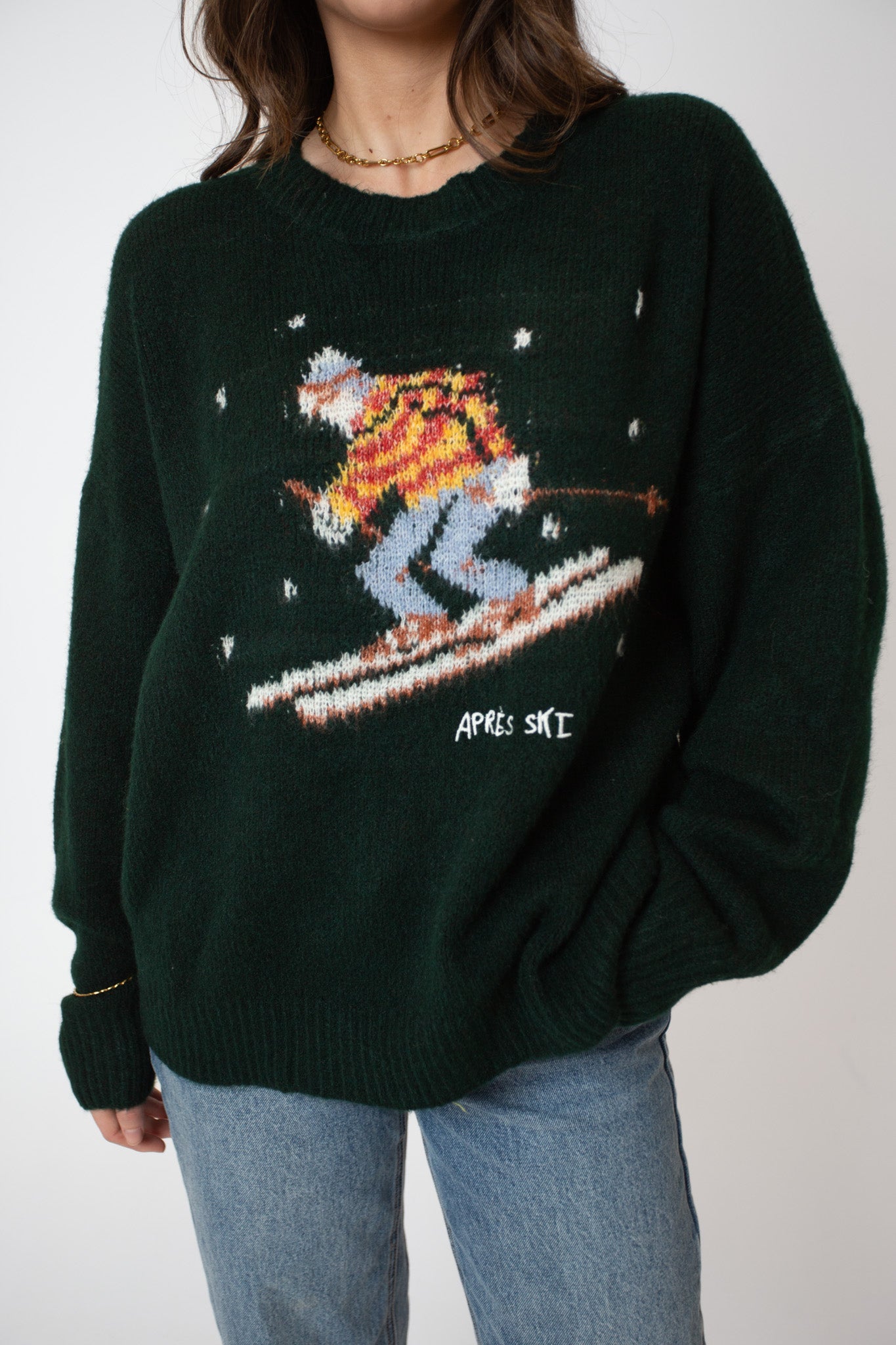 Person wearing a dark green sweater with a skiing design on a plain background
