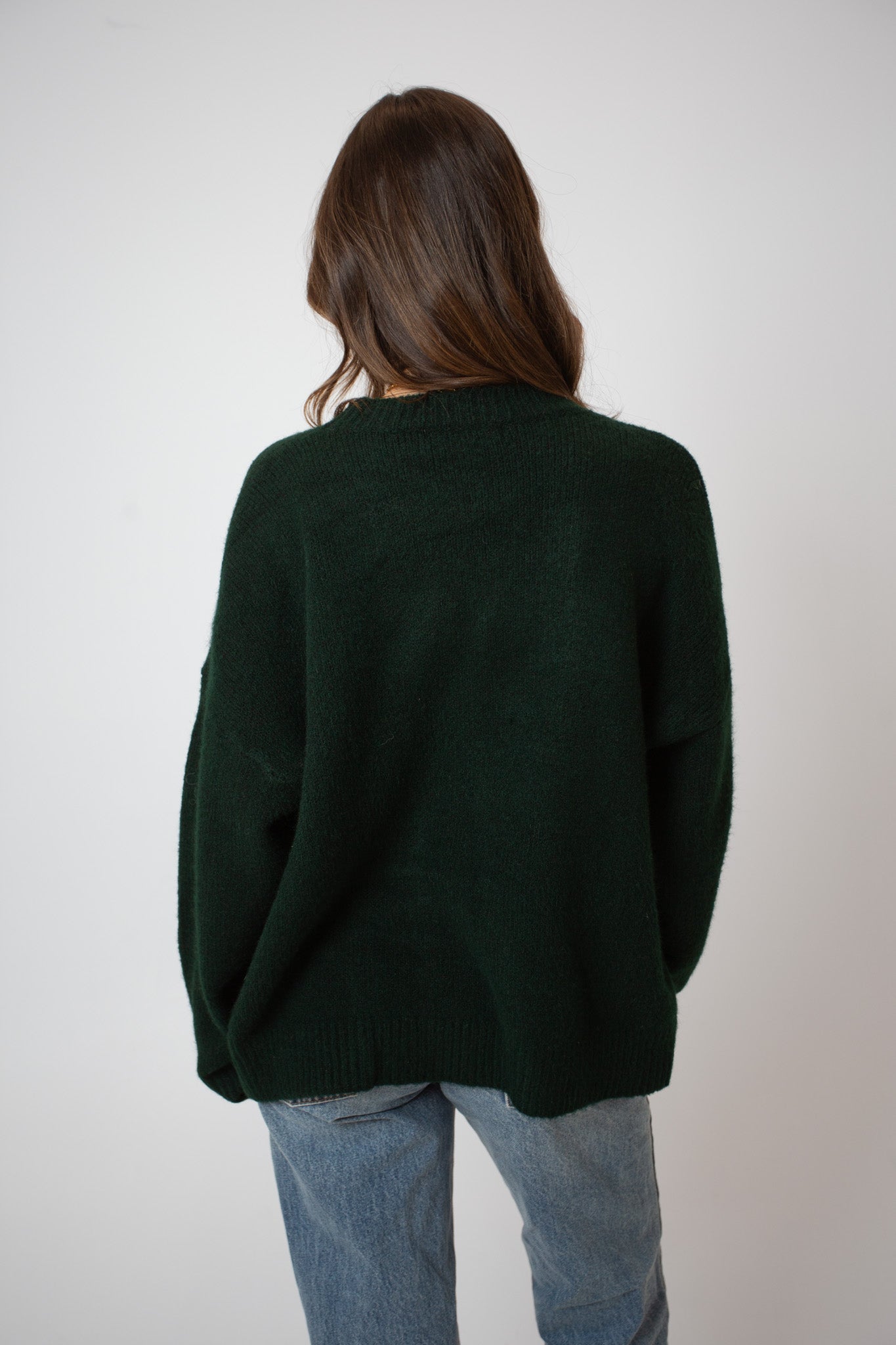 Person wearing a dark green sweater and light blue jeans on a plain background