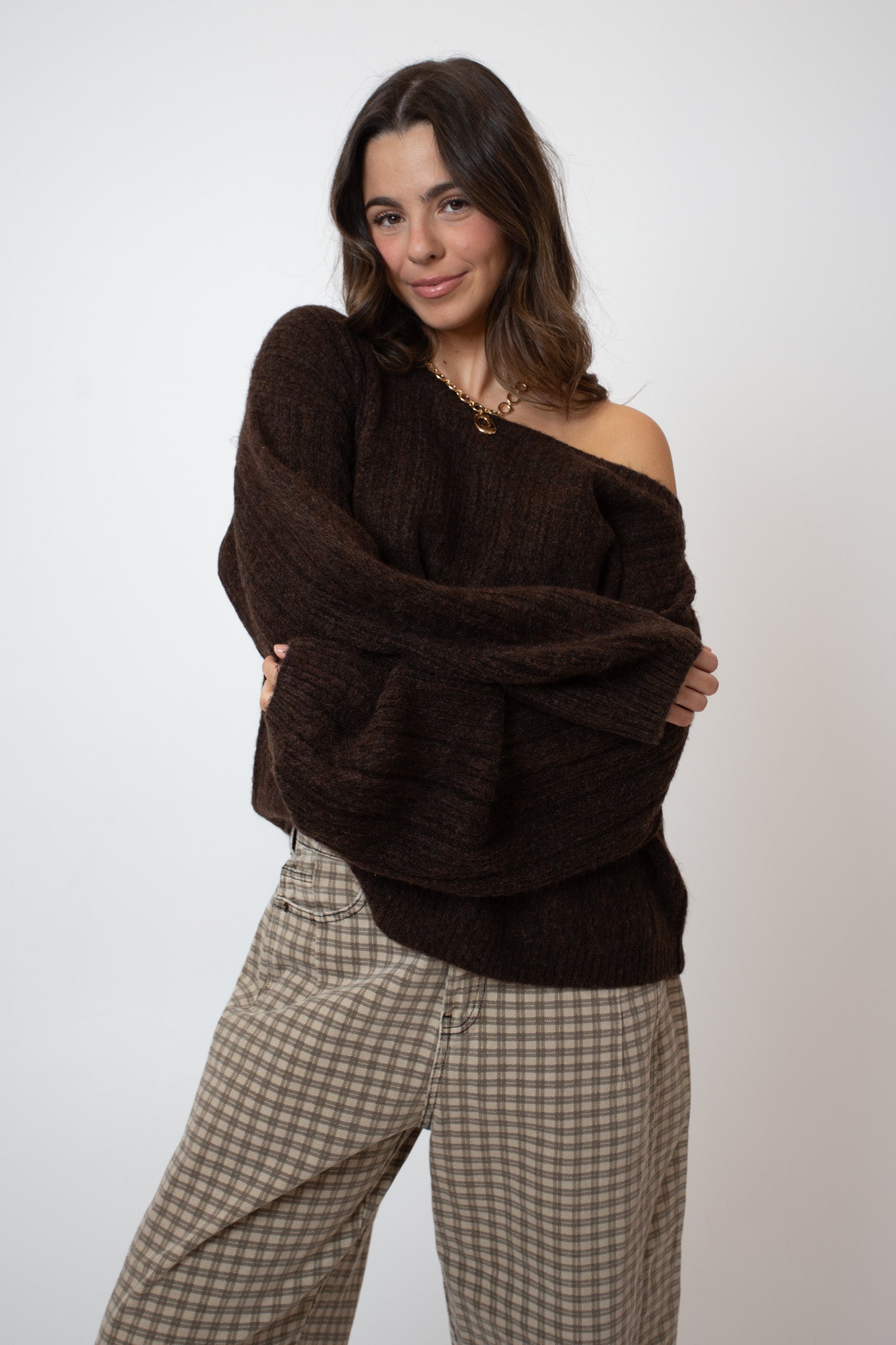 Woman wearing a brown off-shoulder sweater and checkered pants on a white background