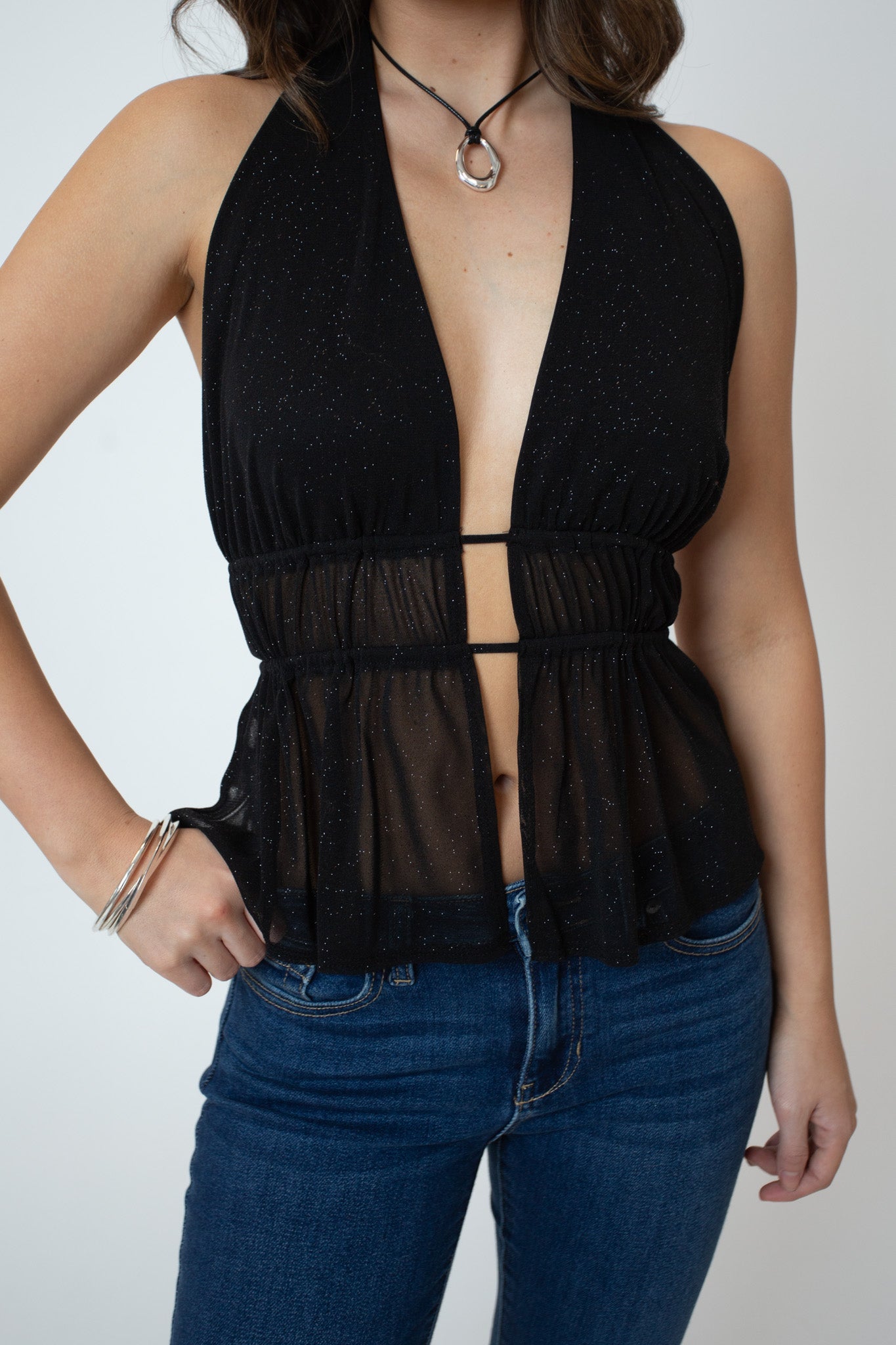 Person wearing a black halter top with sheer panels and blue jeans on a plain background