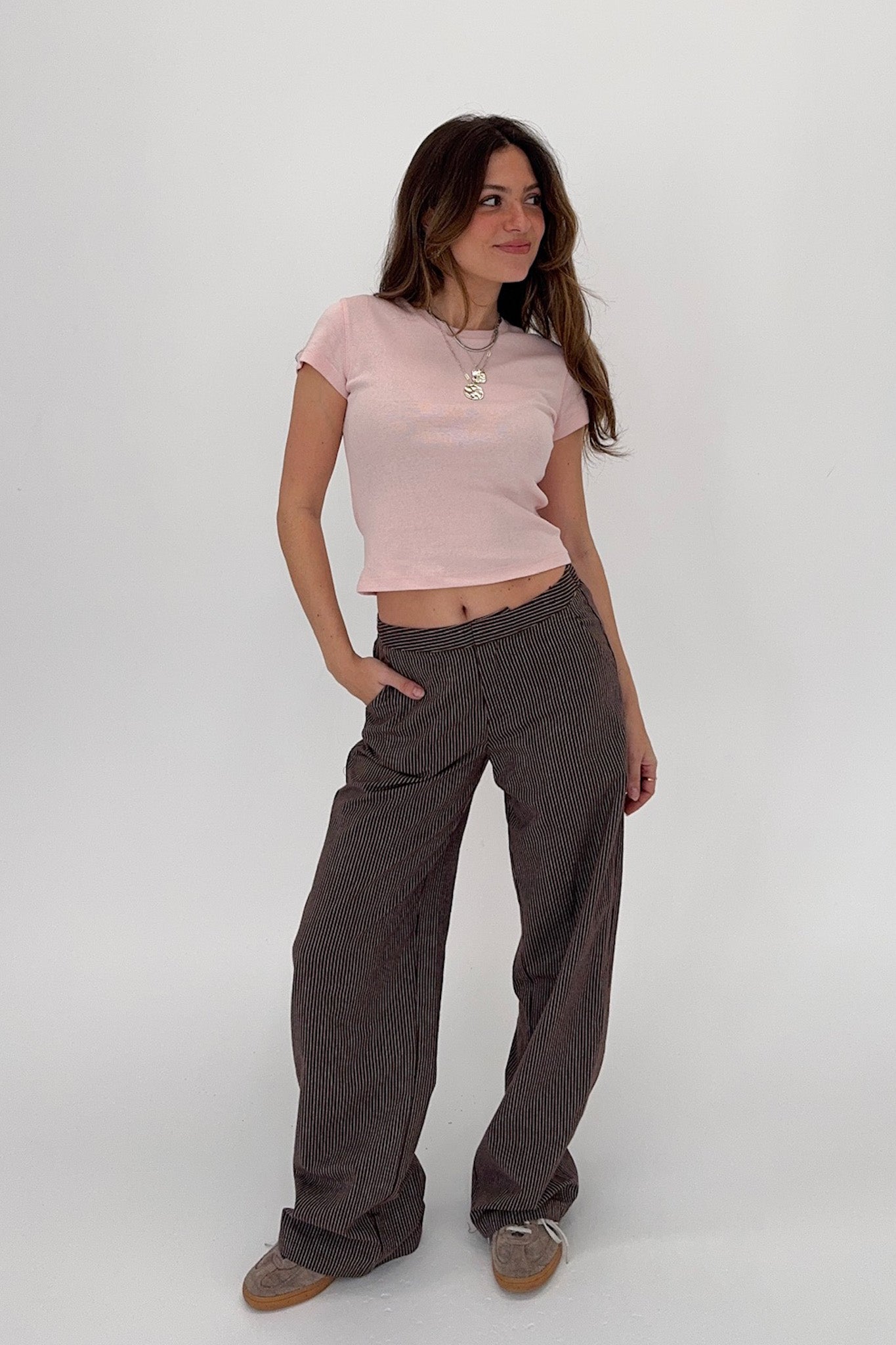 Woman wearing a pink top and brown pants on a white background