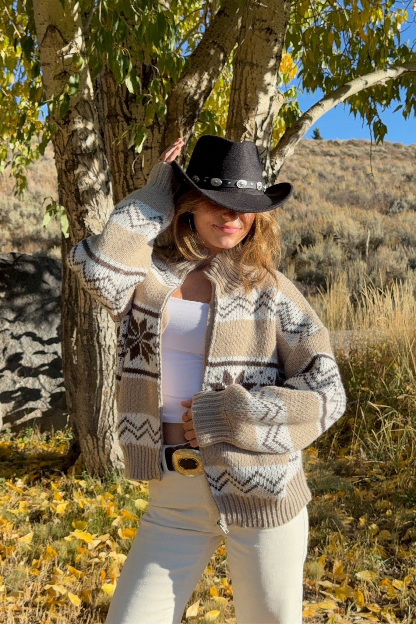 Person wearing a patterned sweater and white pants standing in a natural setting with trees and grass.