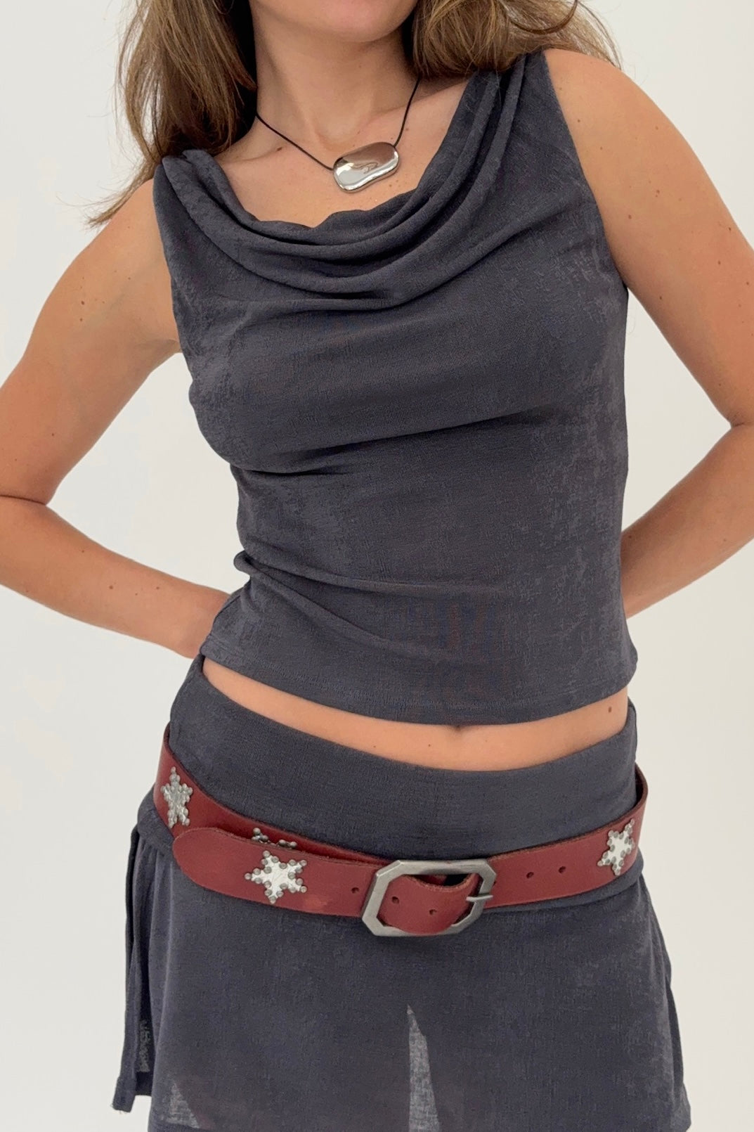 Woman wearing a dark gray sleeveless top and red belt with star designs on a white background