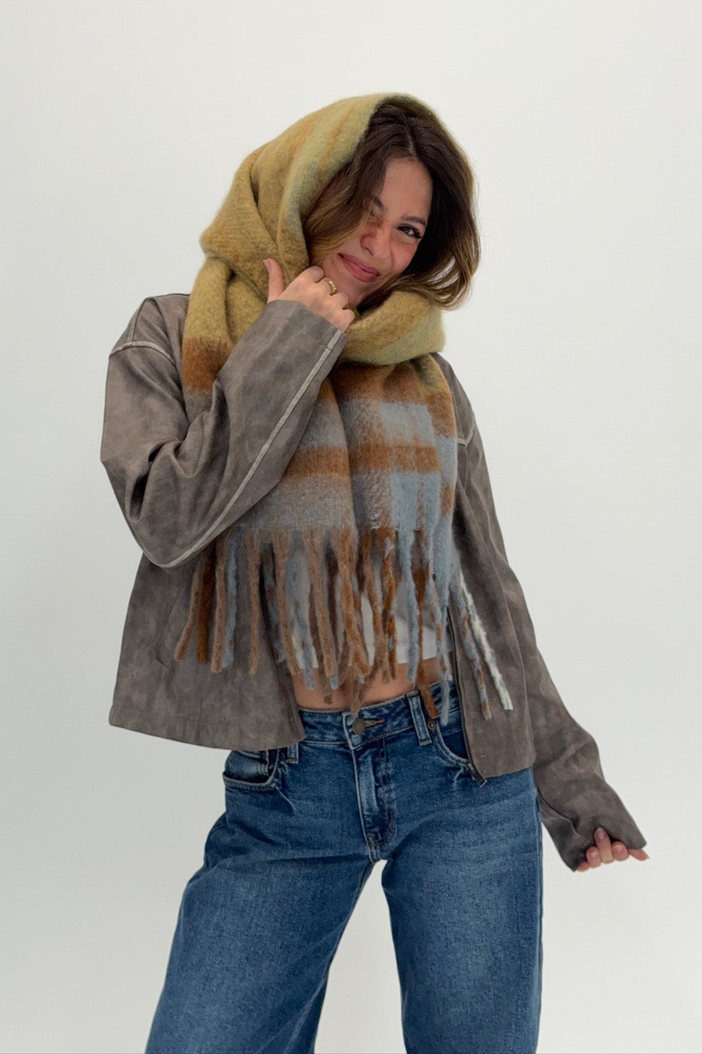 Person wearing a plaid scarf, gray jacket, and blue jeans on a white background