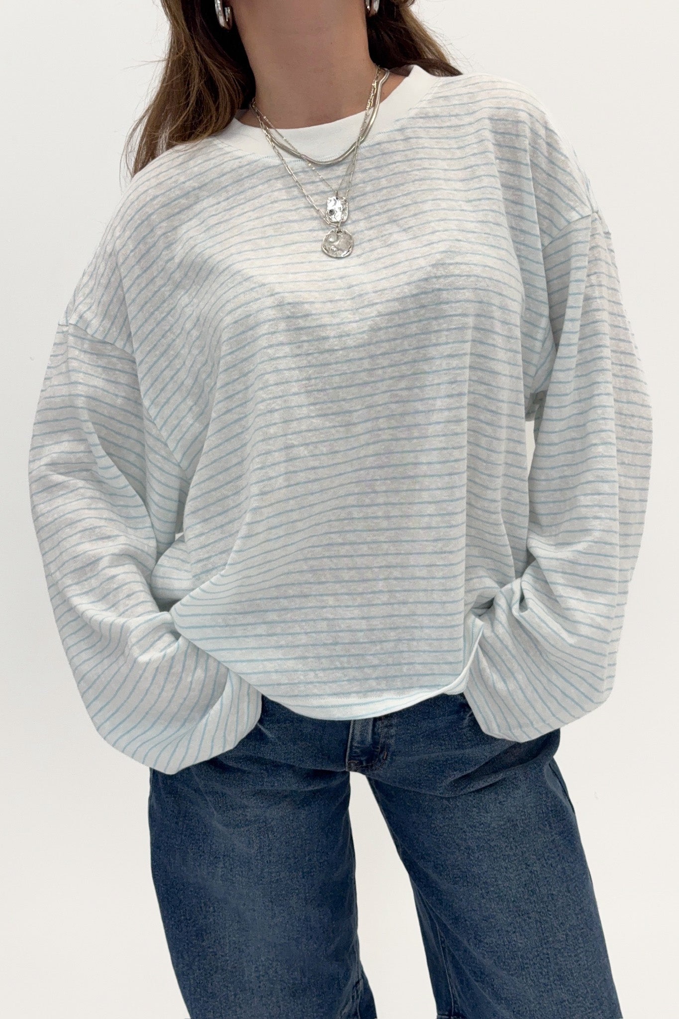 Person wearing a light gray ribbed sweater and blue jeans on a white background