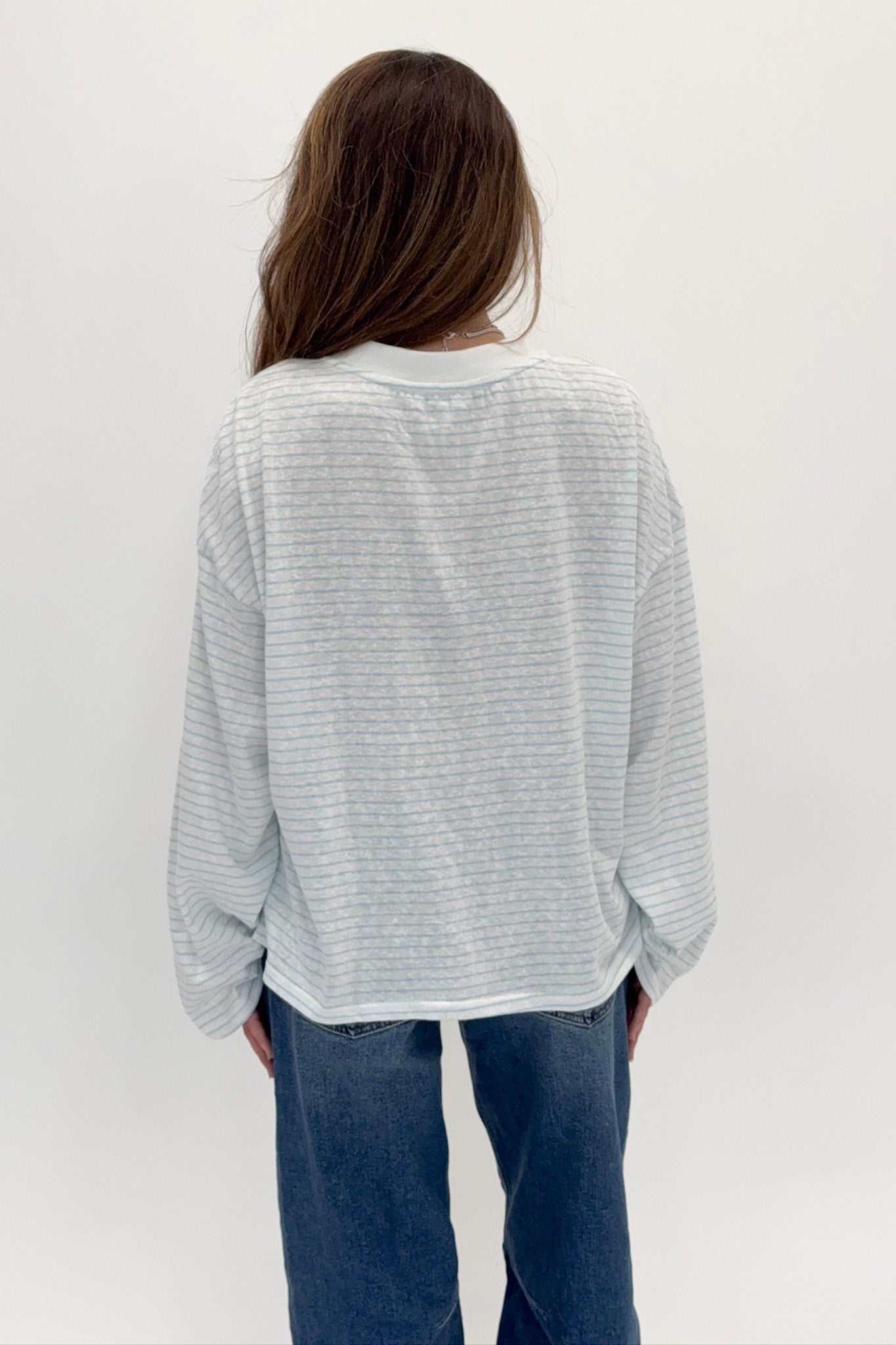 Person wearing a light gray striped shirt and blue jeans against a white background