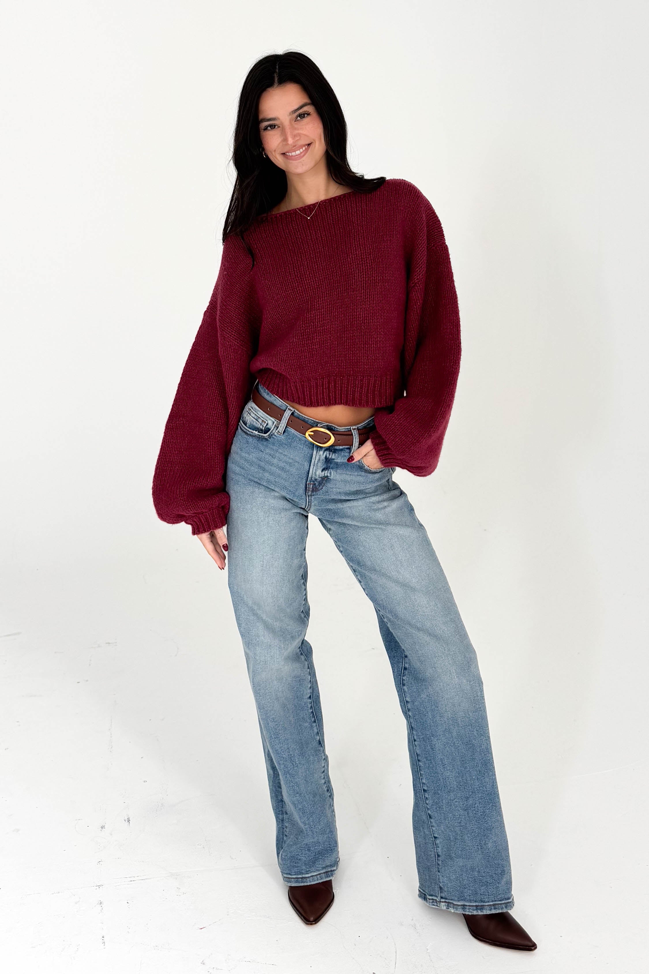 Woman wearing a burgundy sweater and blue jeans on a white background