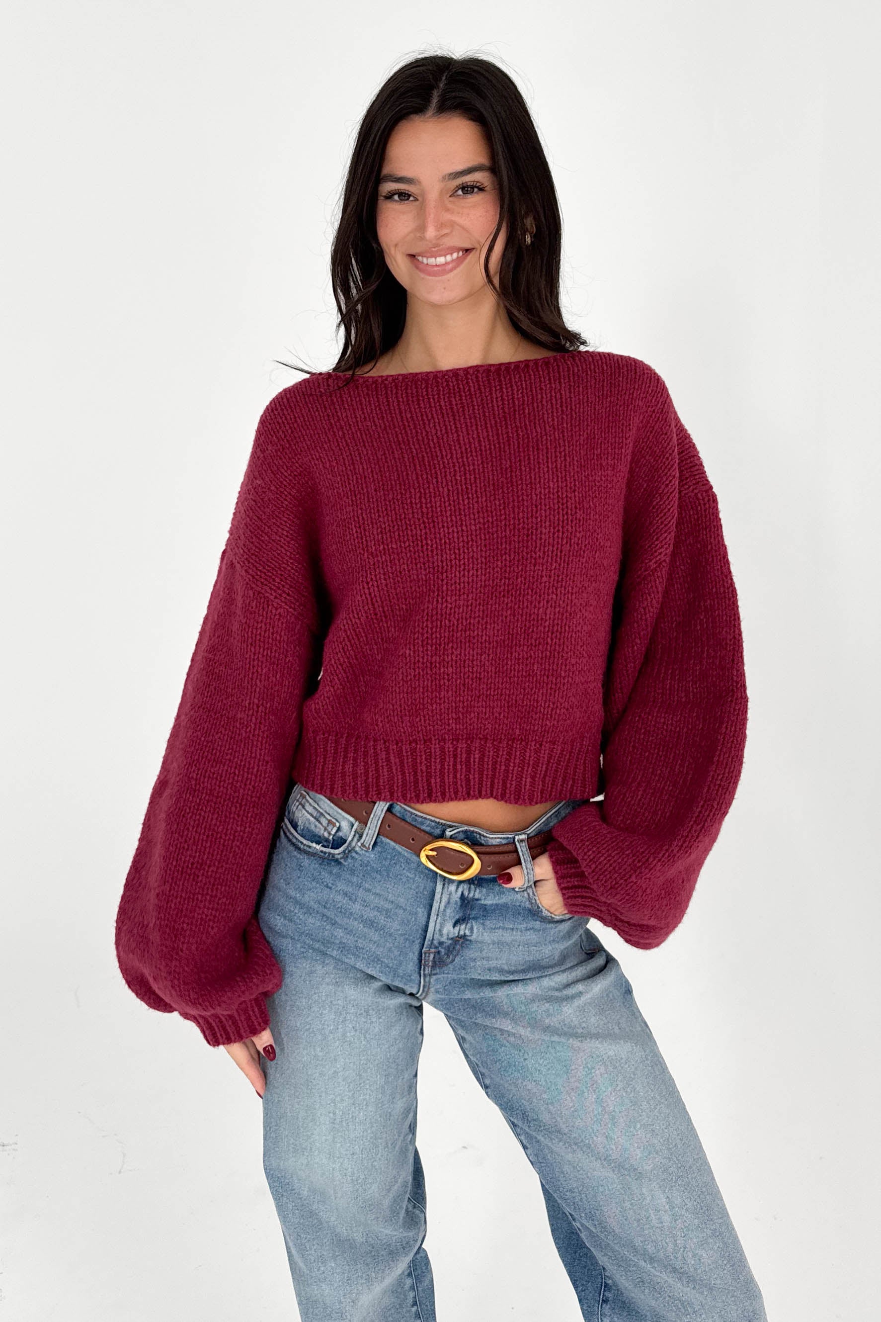 Woman wearing a burgundy sweater and blue jeans on a white background