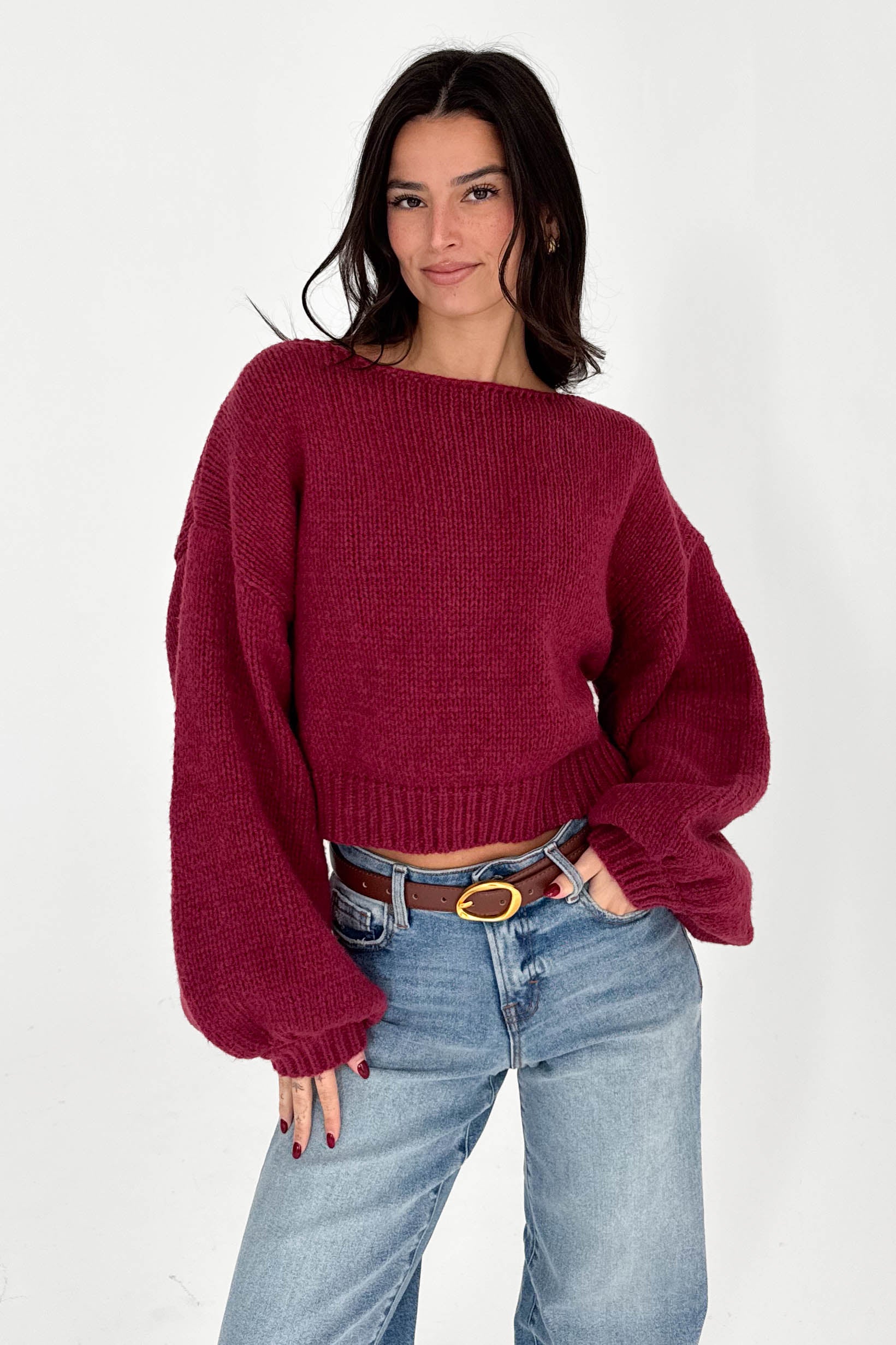 Woman wearing a burgundy sweater and blue jeans against a white background
