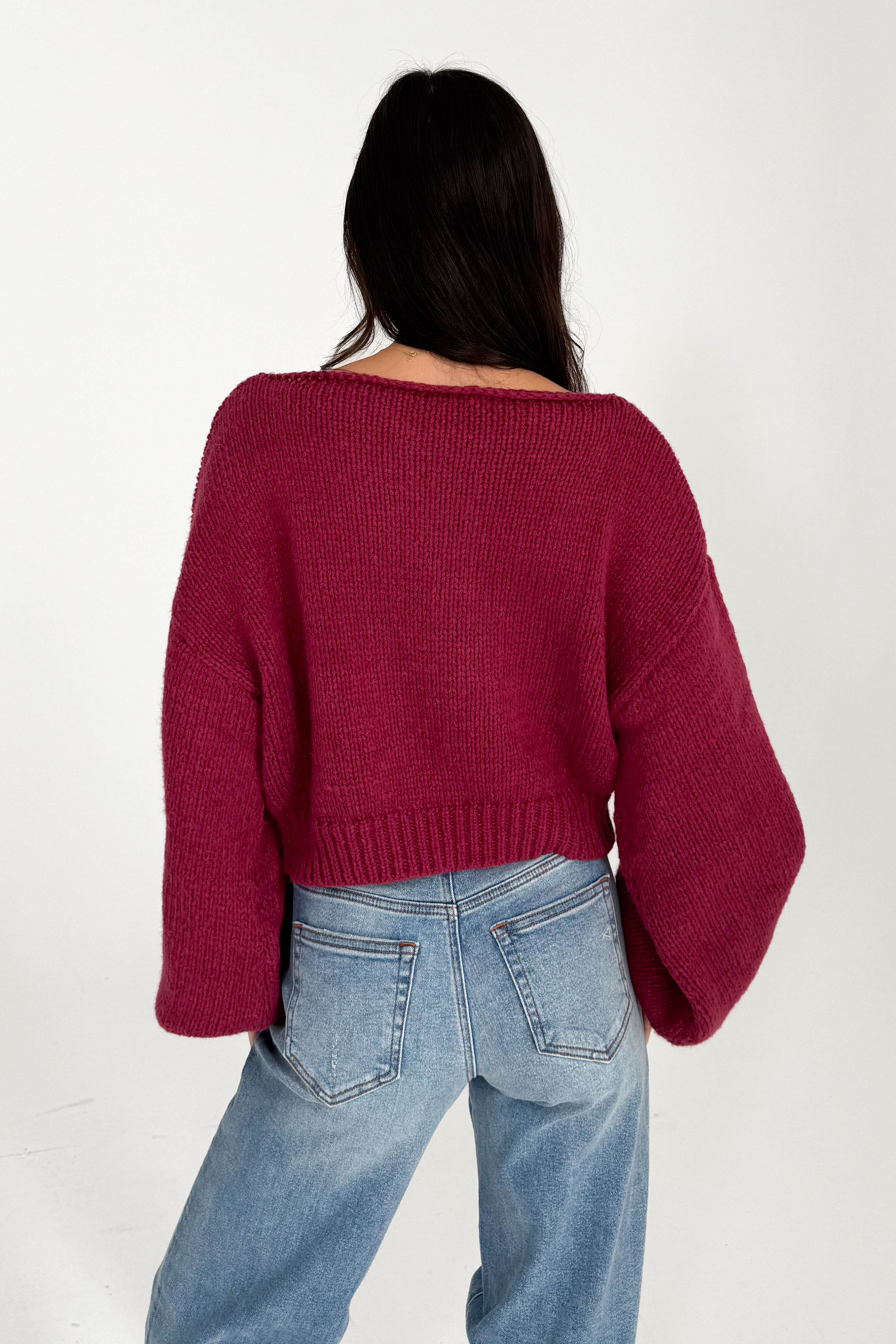 Person wearing a burgundy sweater and blue jeans on a white background