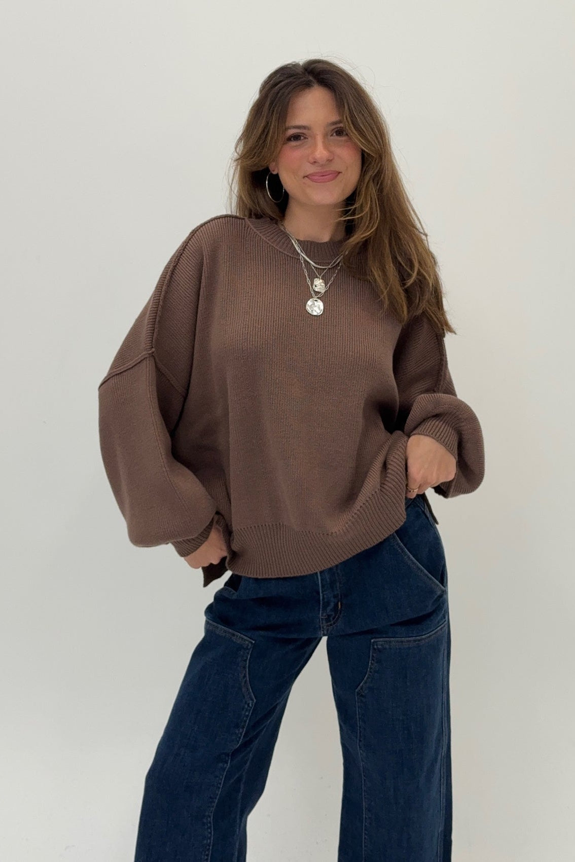 Woman wearing a brown sweater and blue jeans against a white background