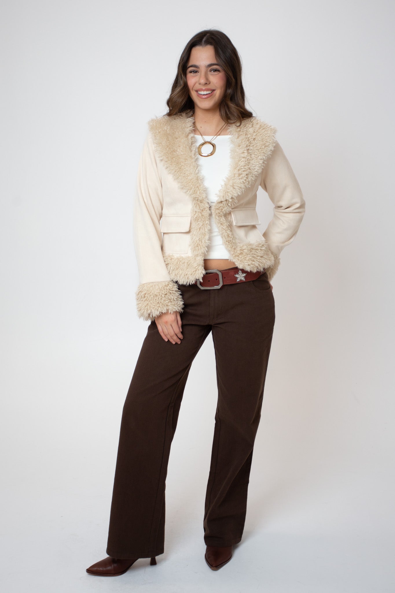Woman wearing a cream fur-trimmed jacket and brown pants on a white background