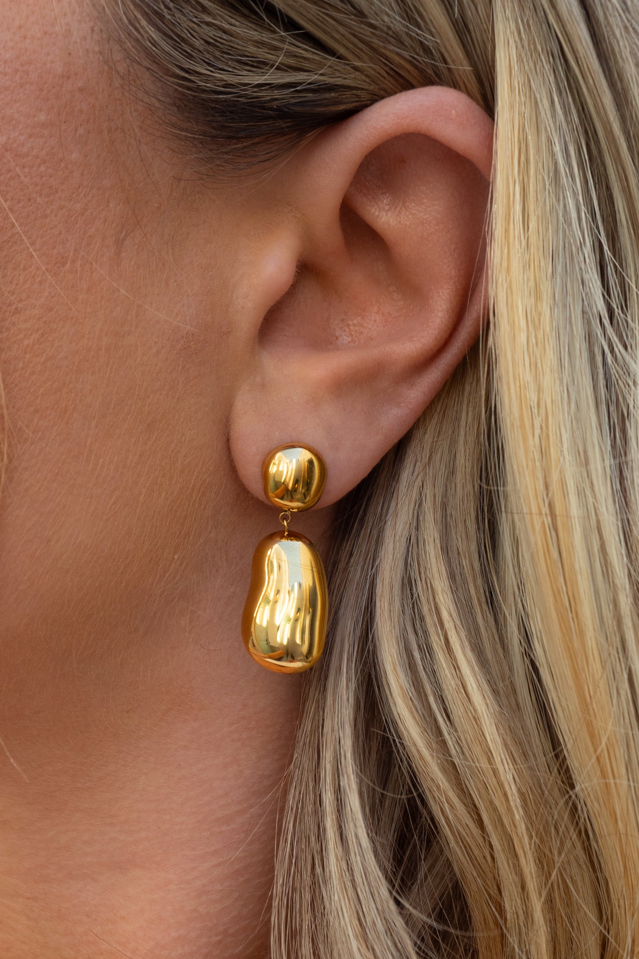Gold earrings worn by a person with blonde hair.
