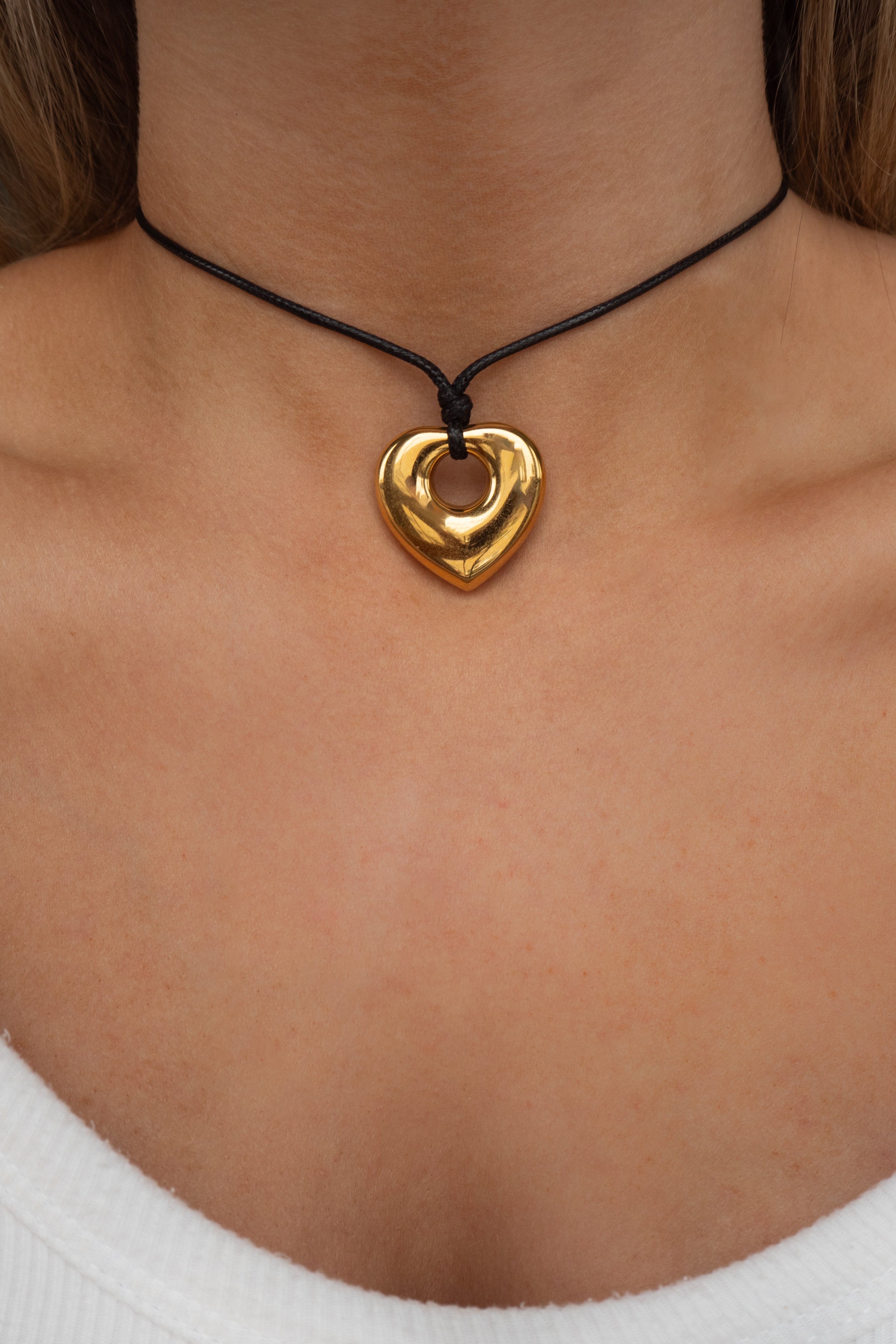 Gold heart-shaped pendant on a black cord necklace worn by a person.