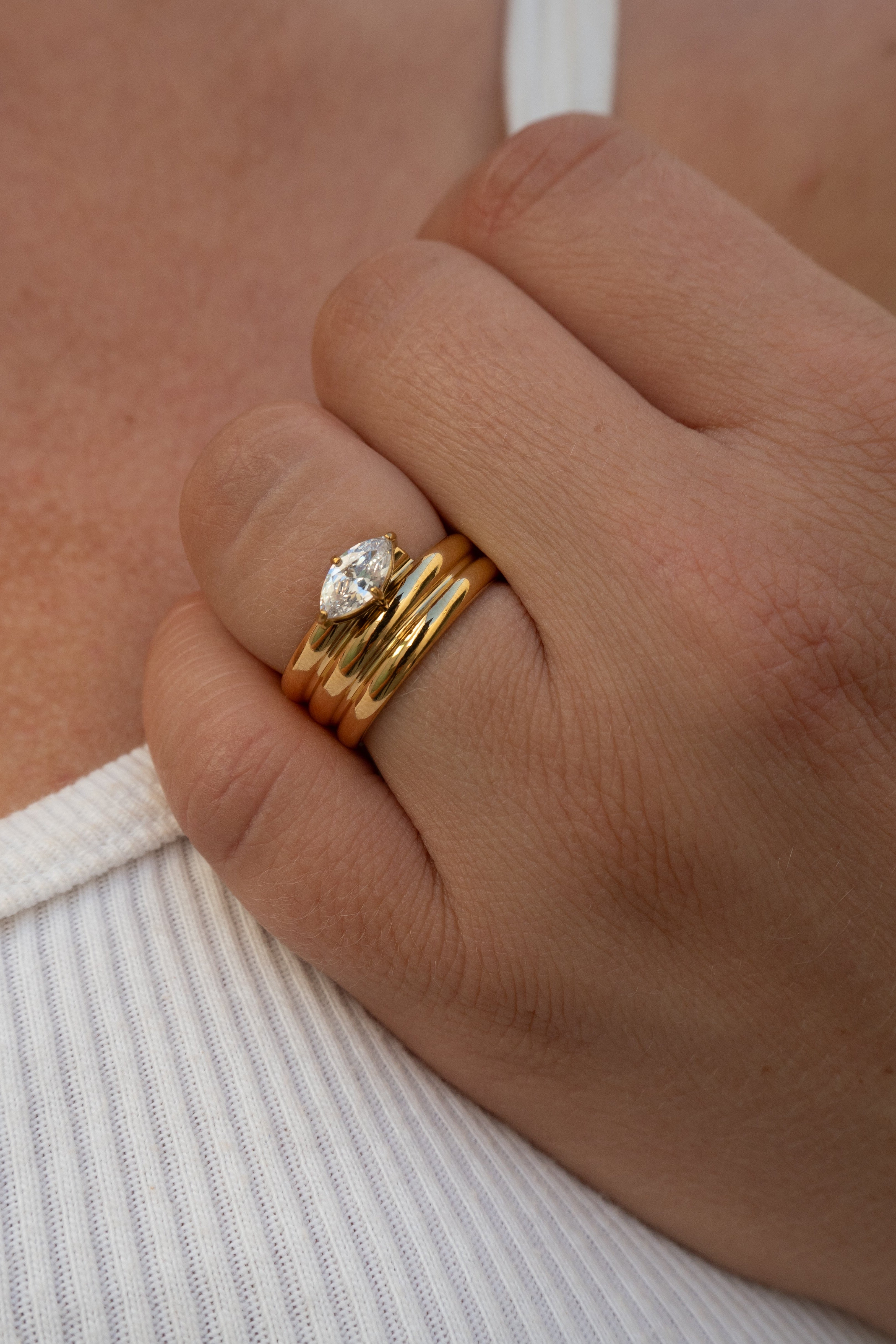 Close-up of a hand wearing two gold rings with a diamond on a neutral background