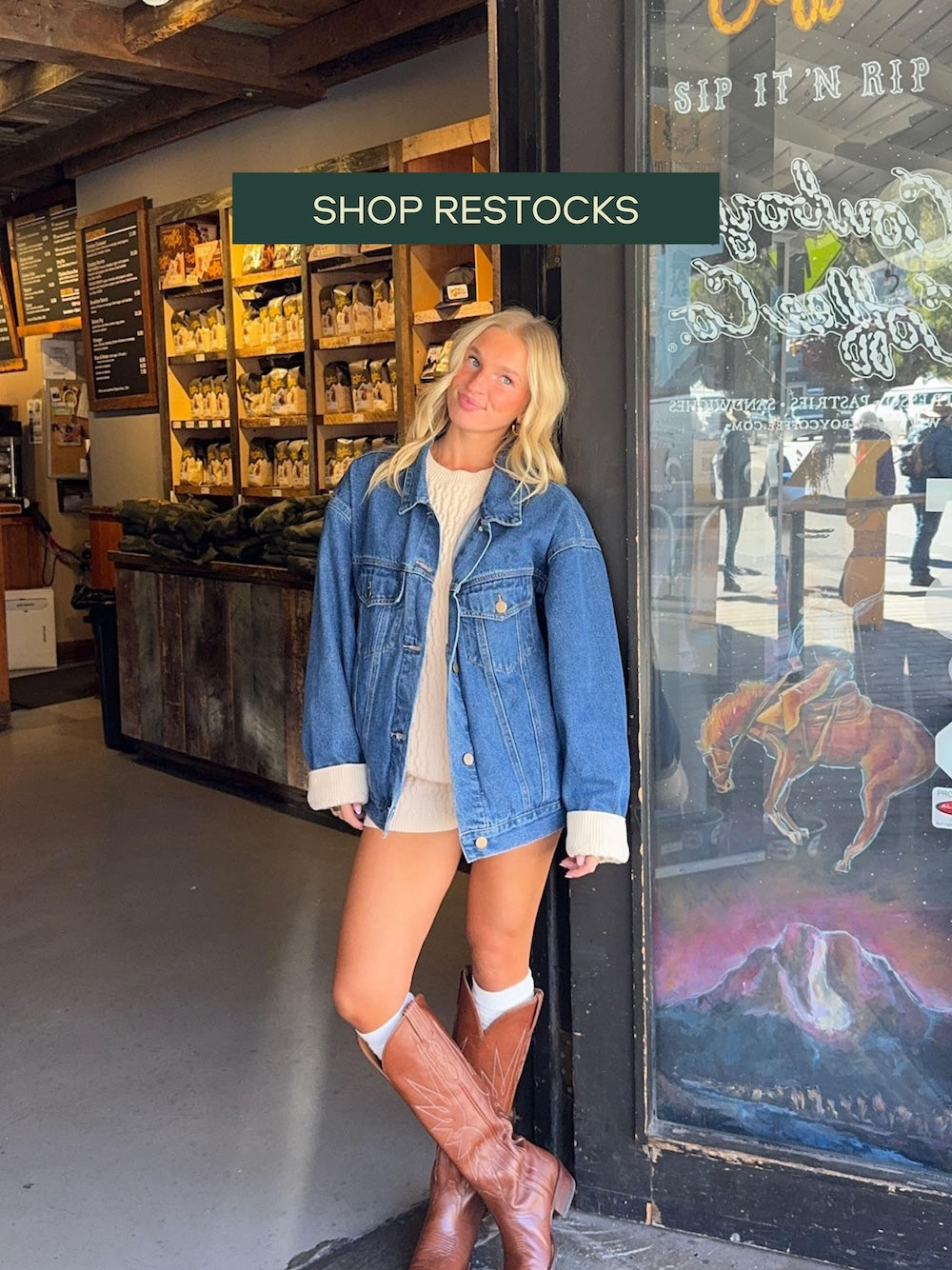 Woman in denim jacket and boots standing outside a store with 'Shop Restocks' text overlay.