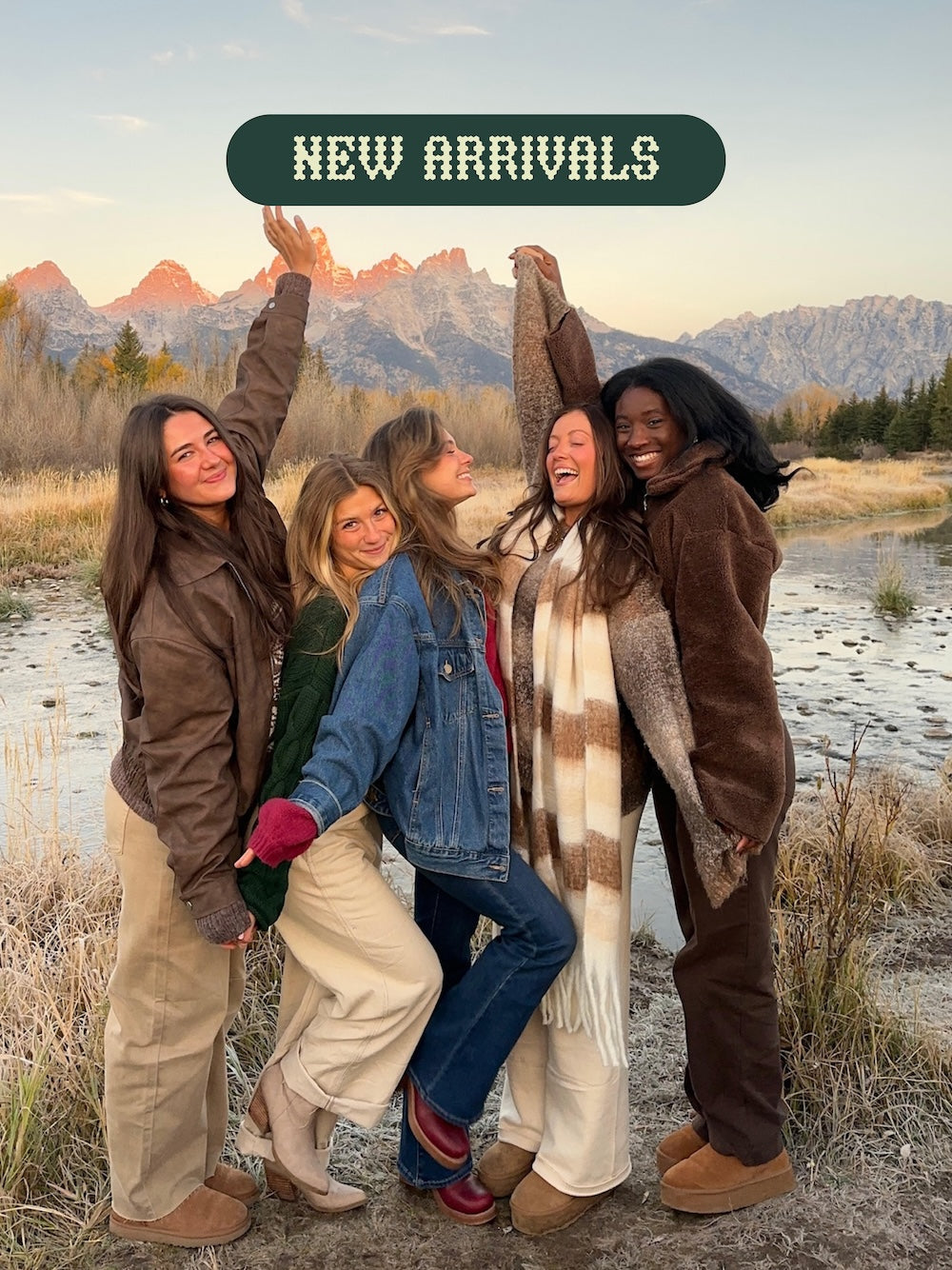 Five women posing together in a scenic outdoor setting with mountains in the background, wearing winter clothing, with New Arrivals written on it.