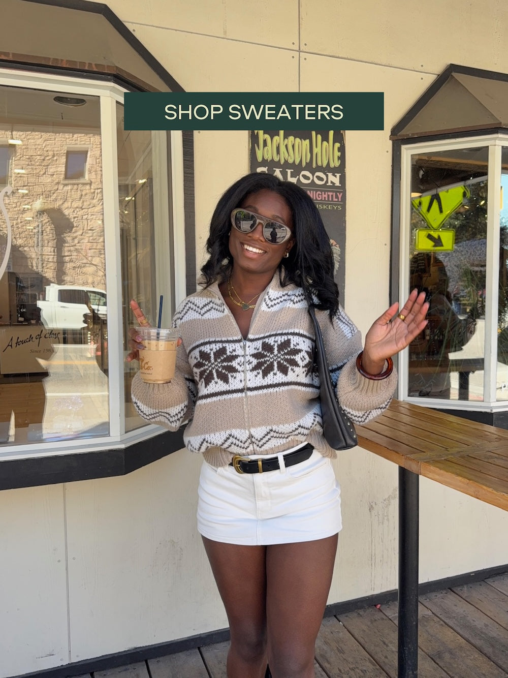 Woman holding a drink outside a store with 'Shop Sweaters' sign above.