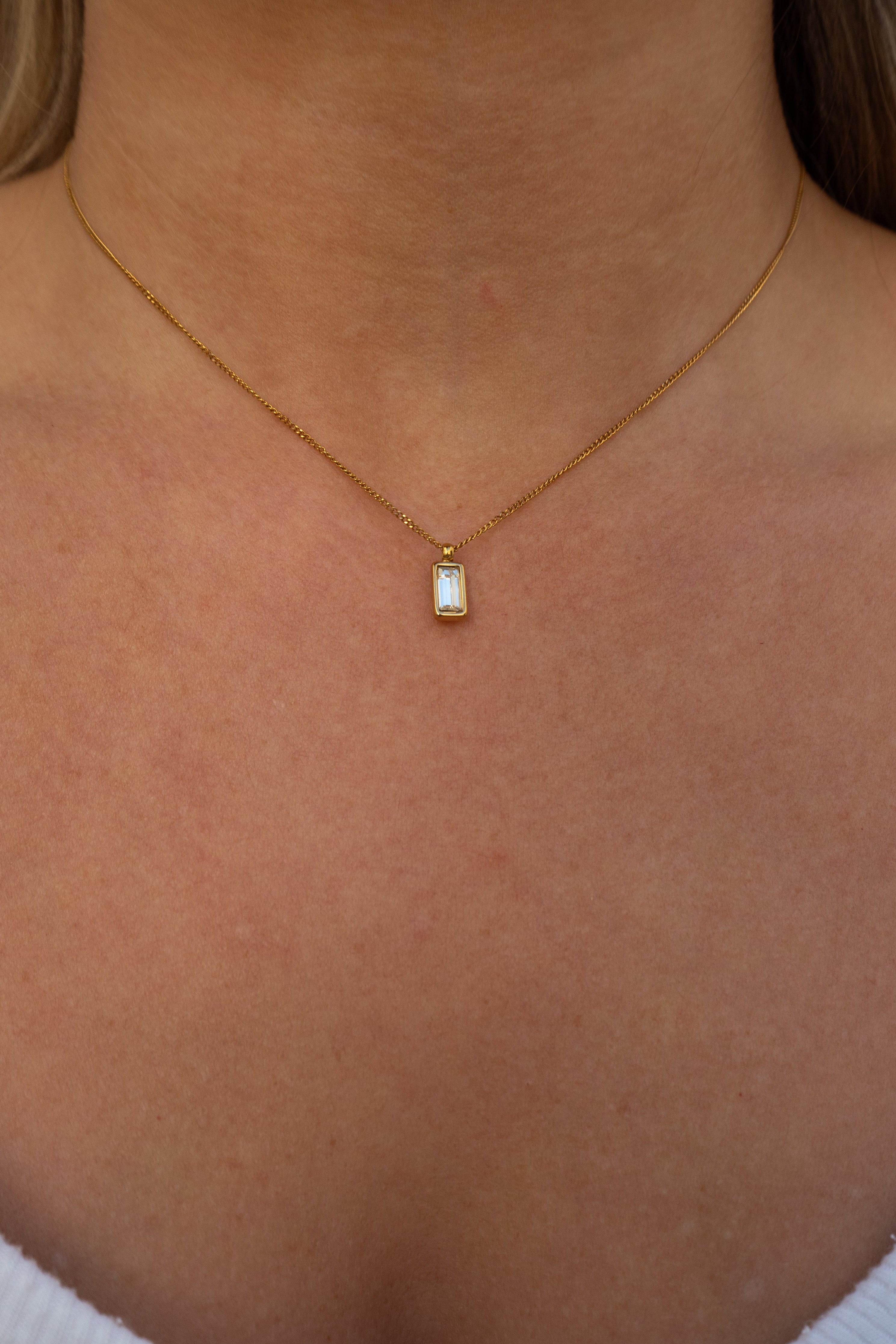 Gold necklace with a small pendant on a person's neck