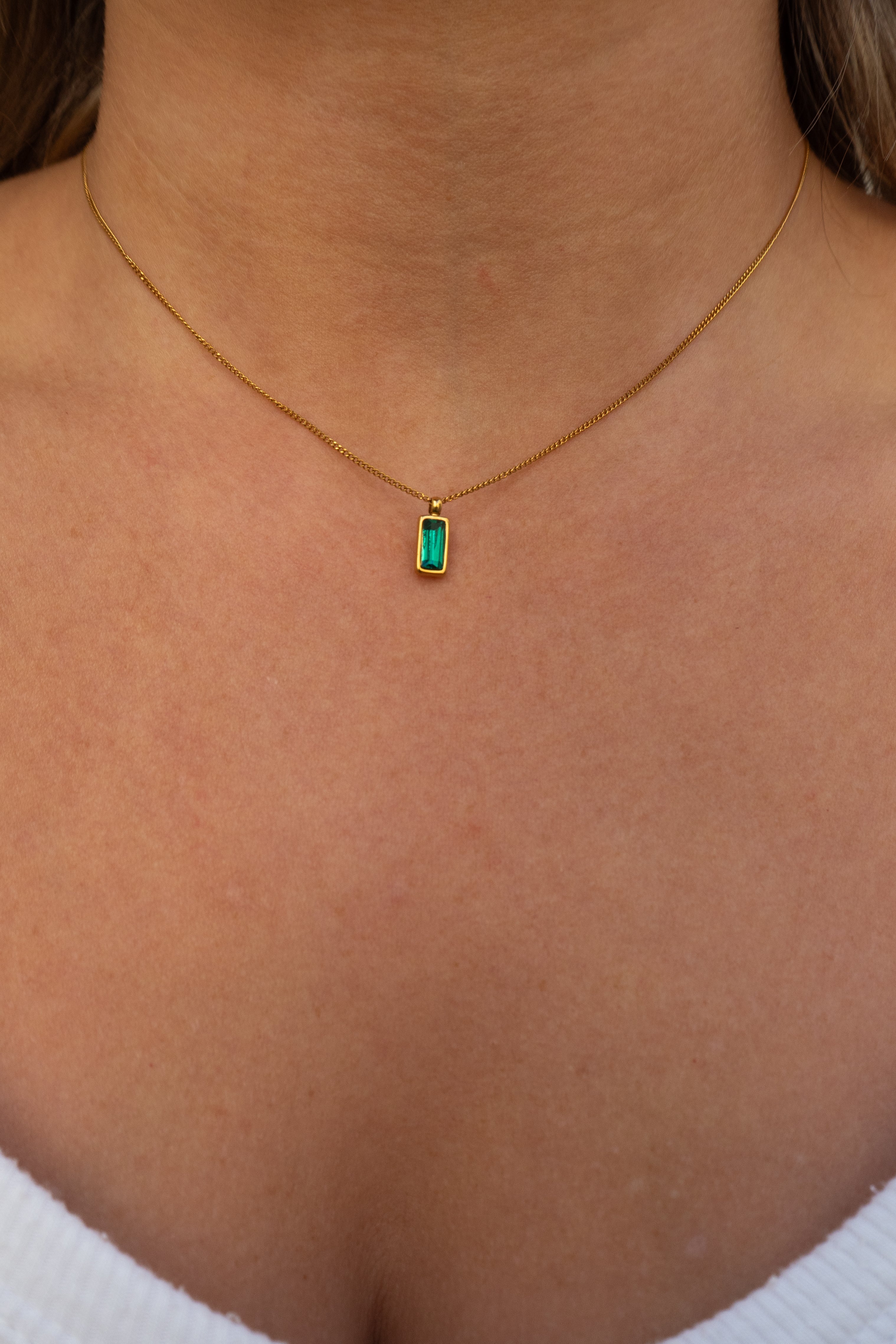 Gold necklace with a green gemstone pendant on a person wearing a white top.