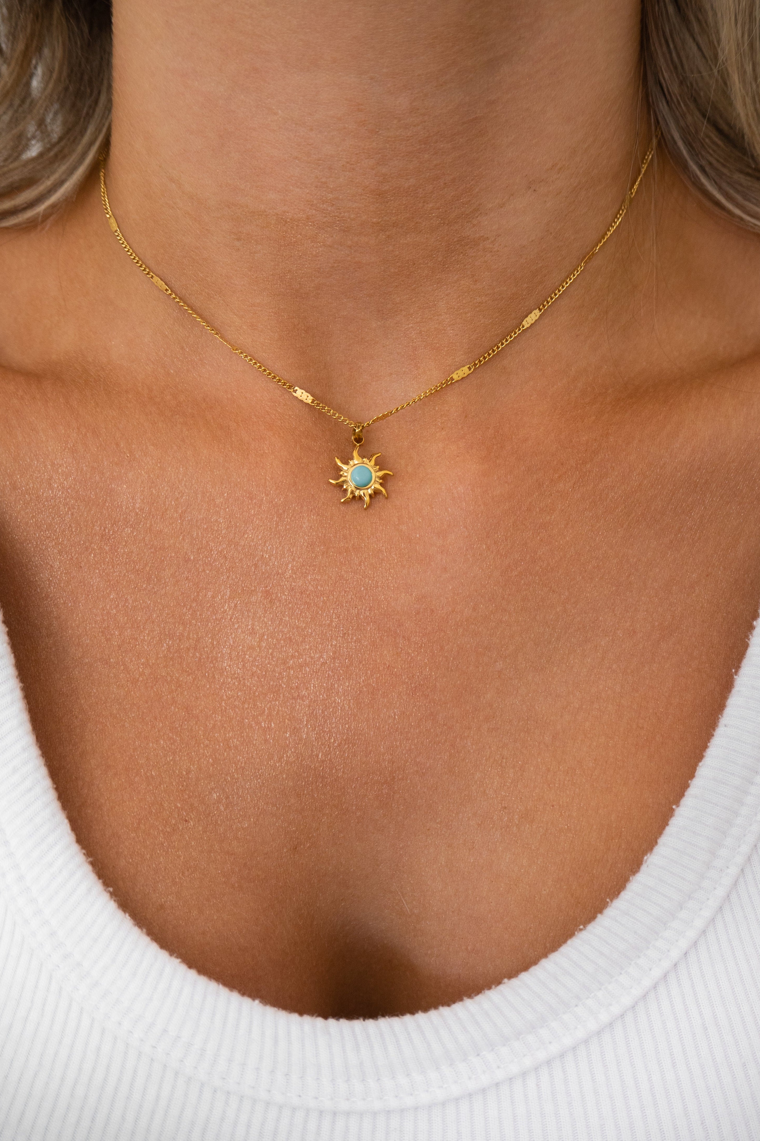 Gold necklace with a sun pendant worn by a person in a white top