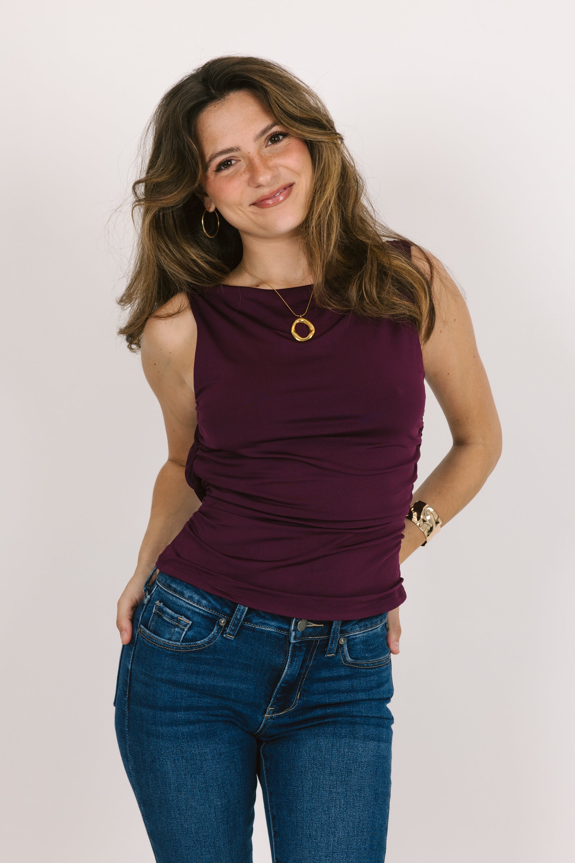 Woman wearing a purple tank top and blue jeans against a white background