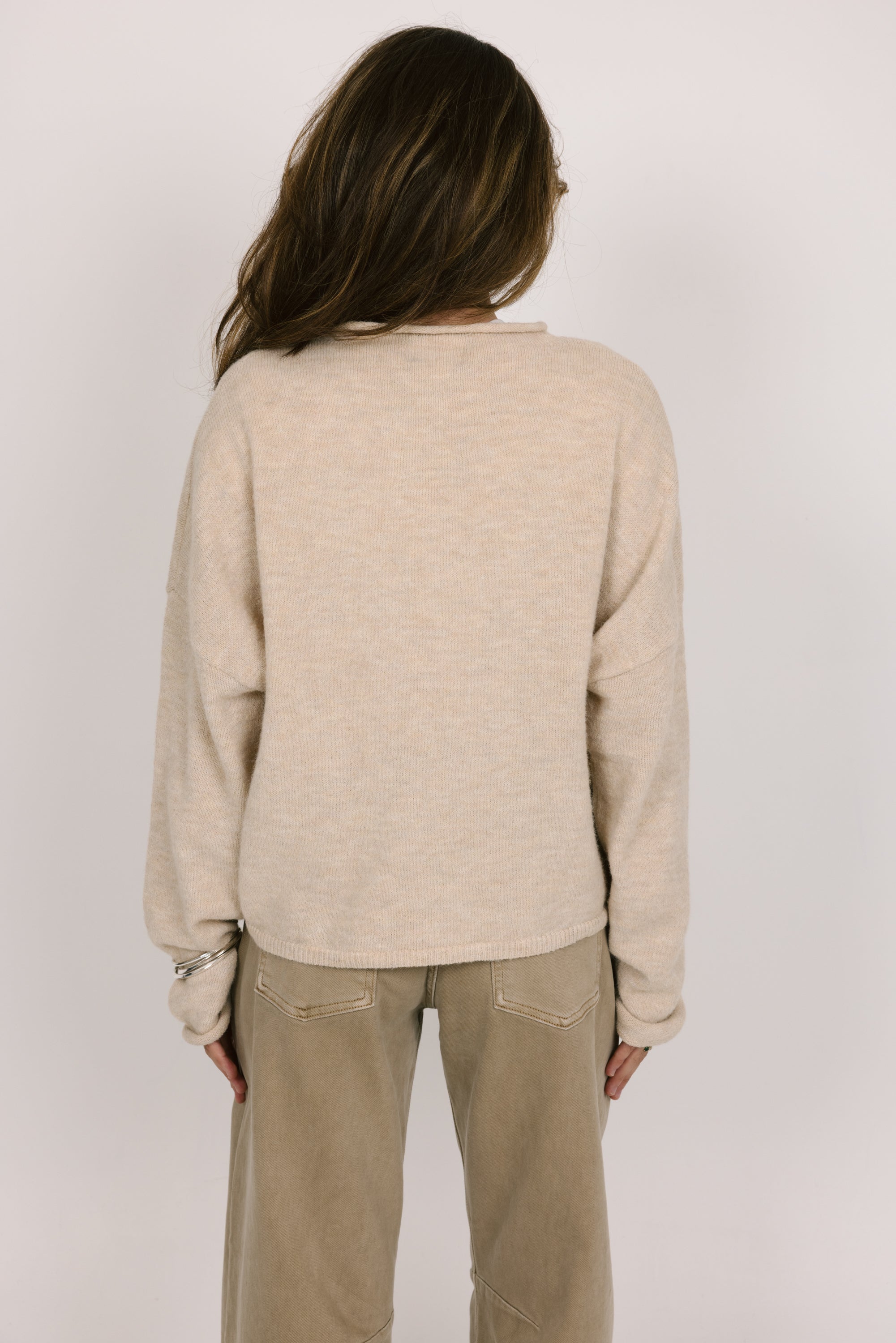 Person wearing a beige sweater and pants on a plain background