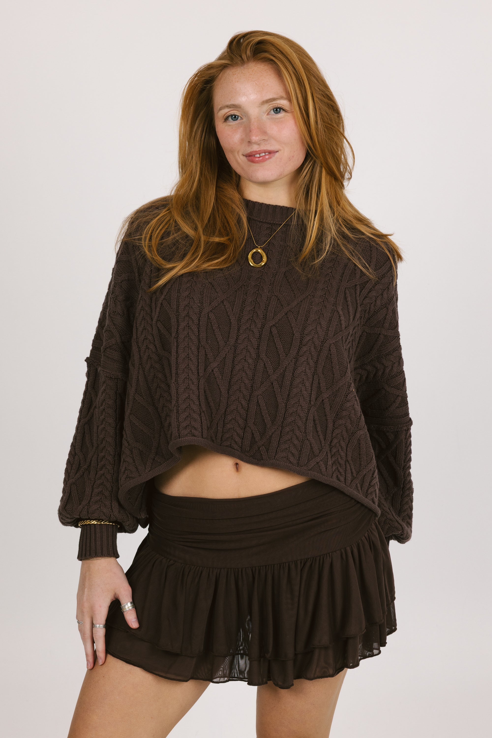 Woman wearing a brown cable knit sweater and skirt on a white background
