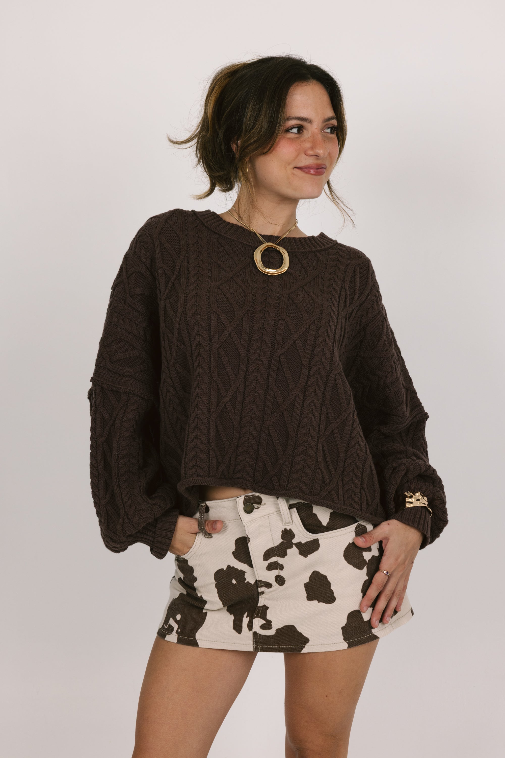 Woman wearing a brown sweater and patterned skirt against a white background