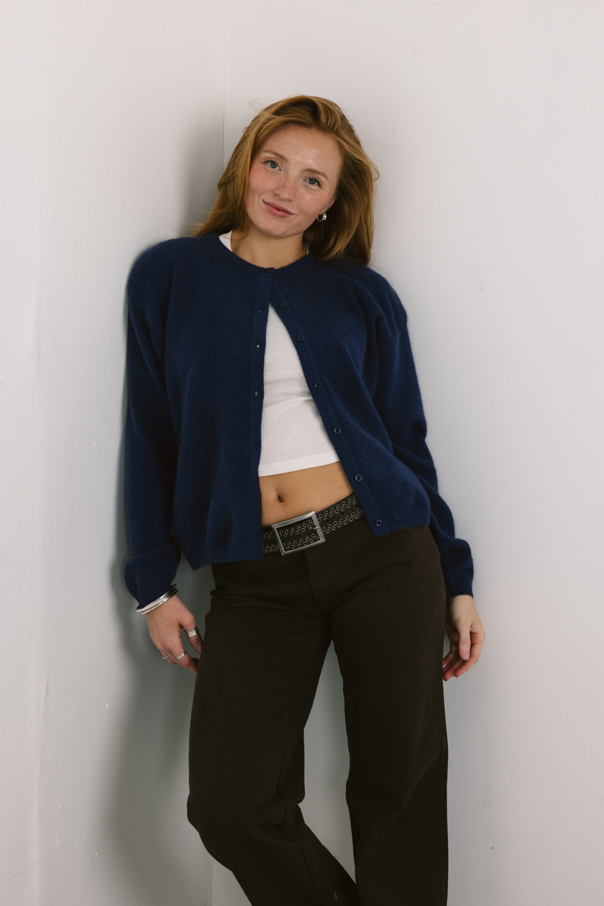 Woman wearing a navy blue cardigan over a white shirt and dark pants against a plain background